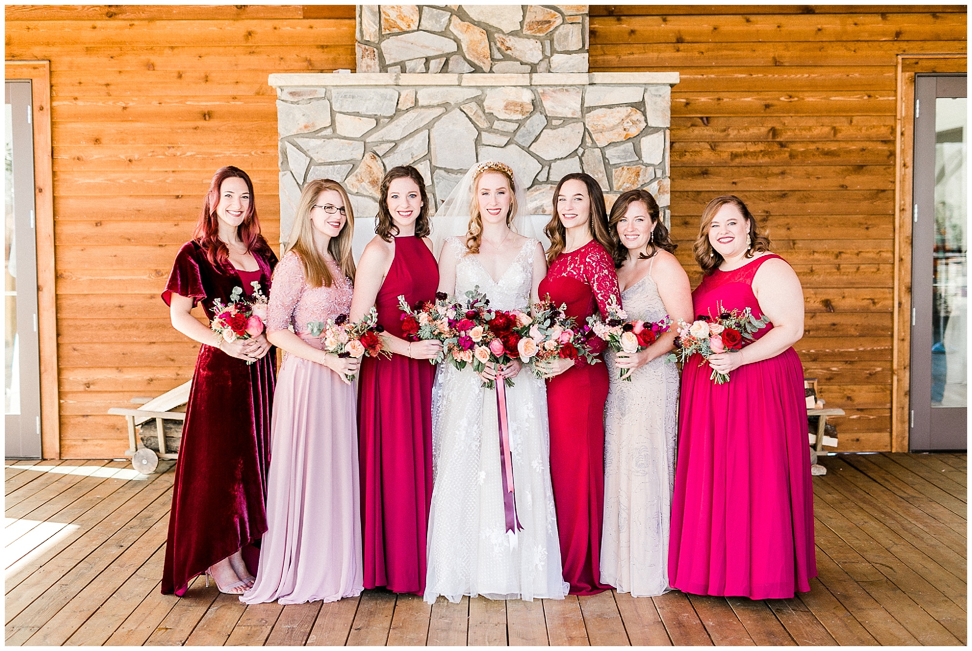 bride poses with bridesmaids in mismatched red and pink gowns