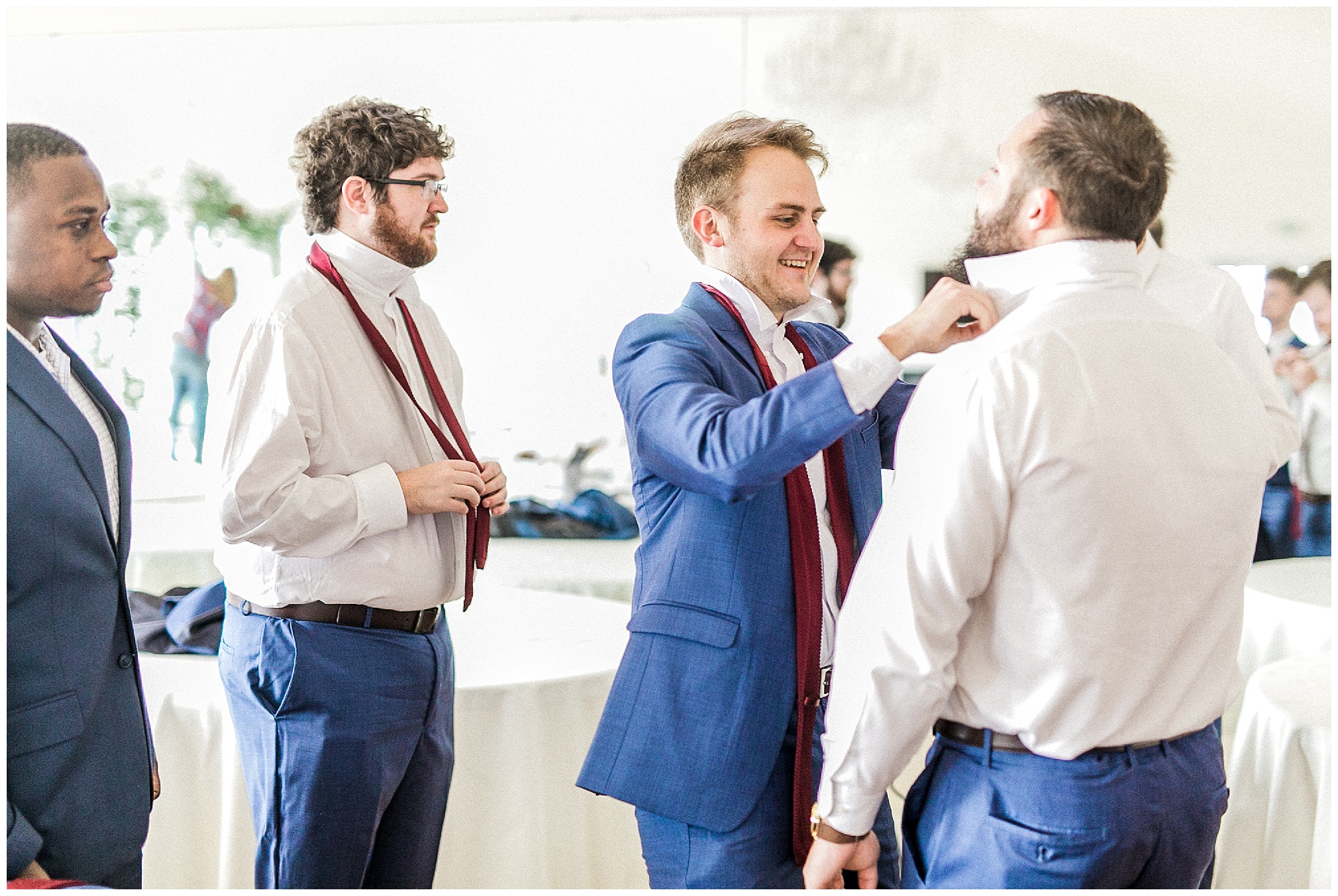 groomsmen help groom with navy suit and burgundy tie