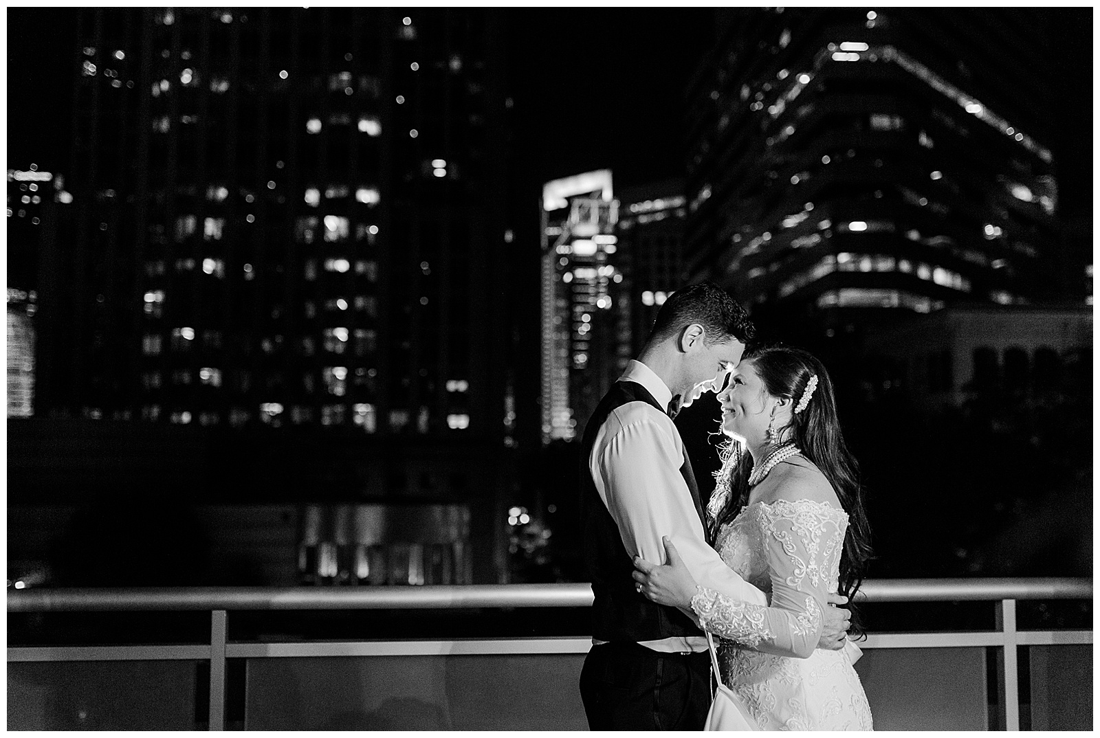 💍 bride groom outdoor black and white portrait after wedding with downtown city lights in background 👰 Bride: lace wedding dress with rhinestone belt rhinestone barrette in hair down with pearls 🤵 Groom: black tux tuxedo and purple flower boutonnière 💍 Bright Colorful Summer City Wedding in Charlotte, NC with Taryn and Ryan | Kevyn Dixon Photography