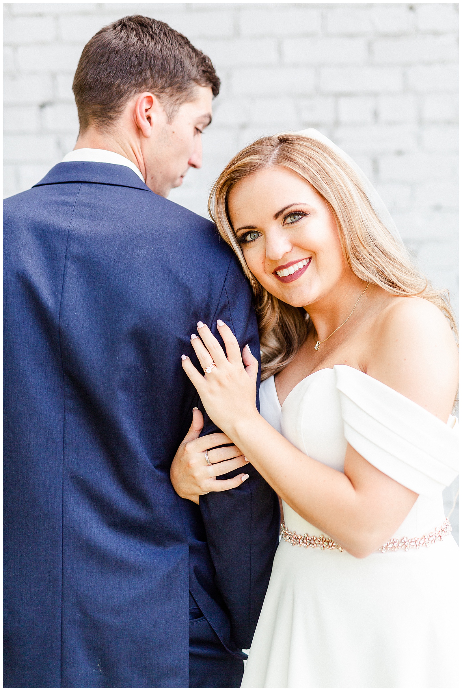 Stunning Modern Bride and Groom with off shoulder wedding dress and blue suit in outdoor portraits in front of white grungy wall from Summer Wedding in Charlotte, NC | Check out the full wedding at KevynDixonPhoto.com