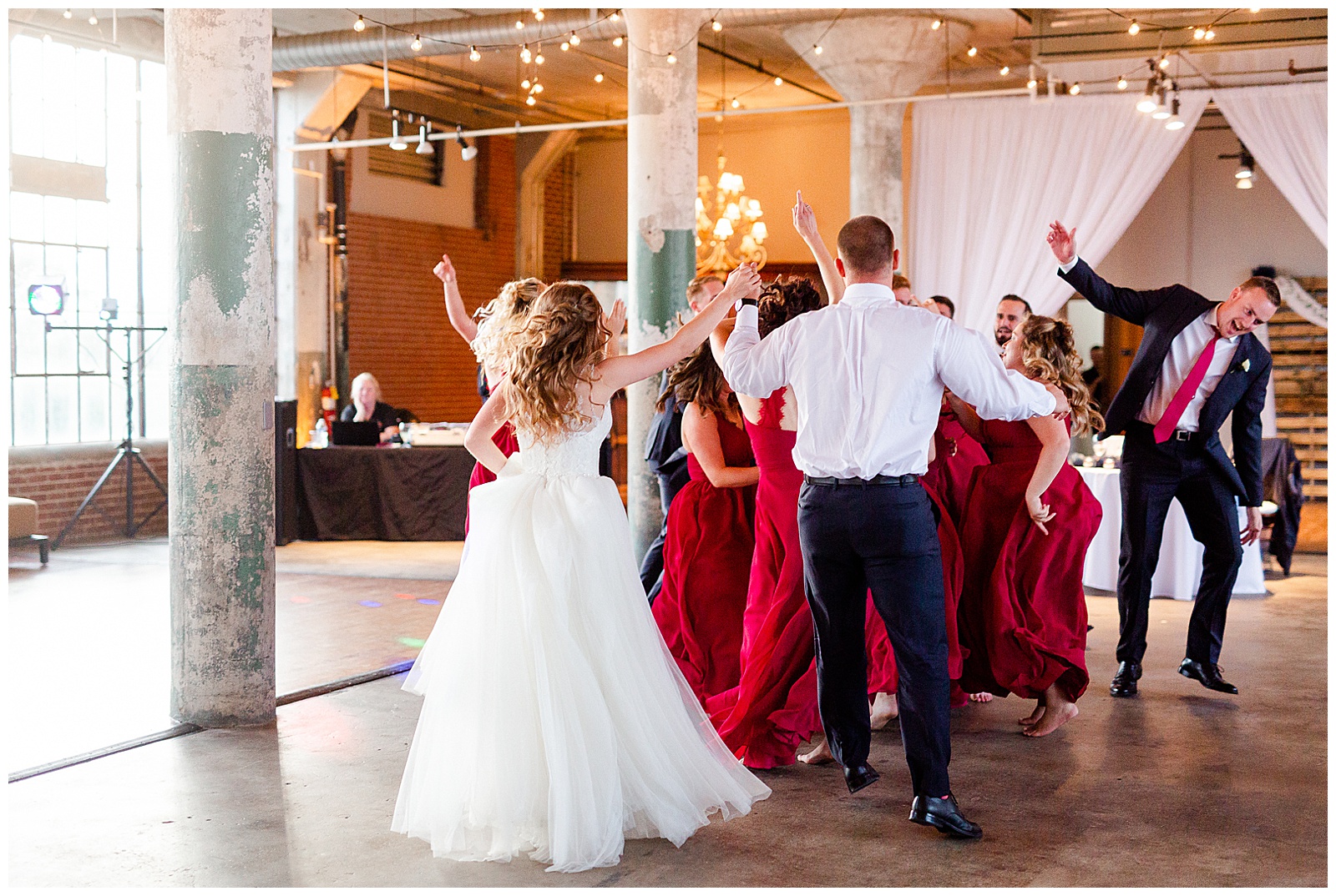 Bride Surprises Groom with Bridesmaid Dance at Rustic Airy Indoor Wedding Venue with fairy lights - Red-Themed Bridesmaid Dress Ideas from Elegant Modern Summer Wedding in Charlotte, NC | check out the full wedding at KevynDixonPhoto.com