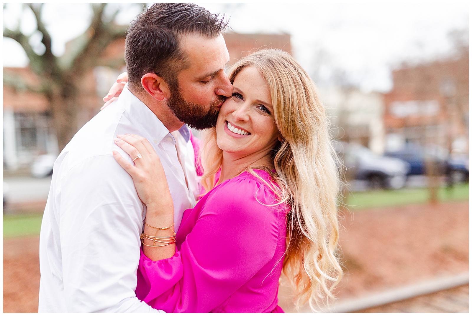 Adorable couple embracing in front of train tracks in downtown Waxhaw, NC Engagement Session with Bright Hot Pink Dress Outfit Ideas