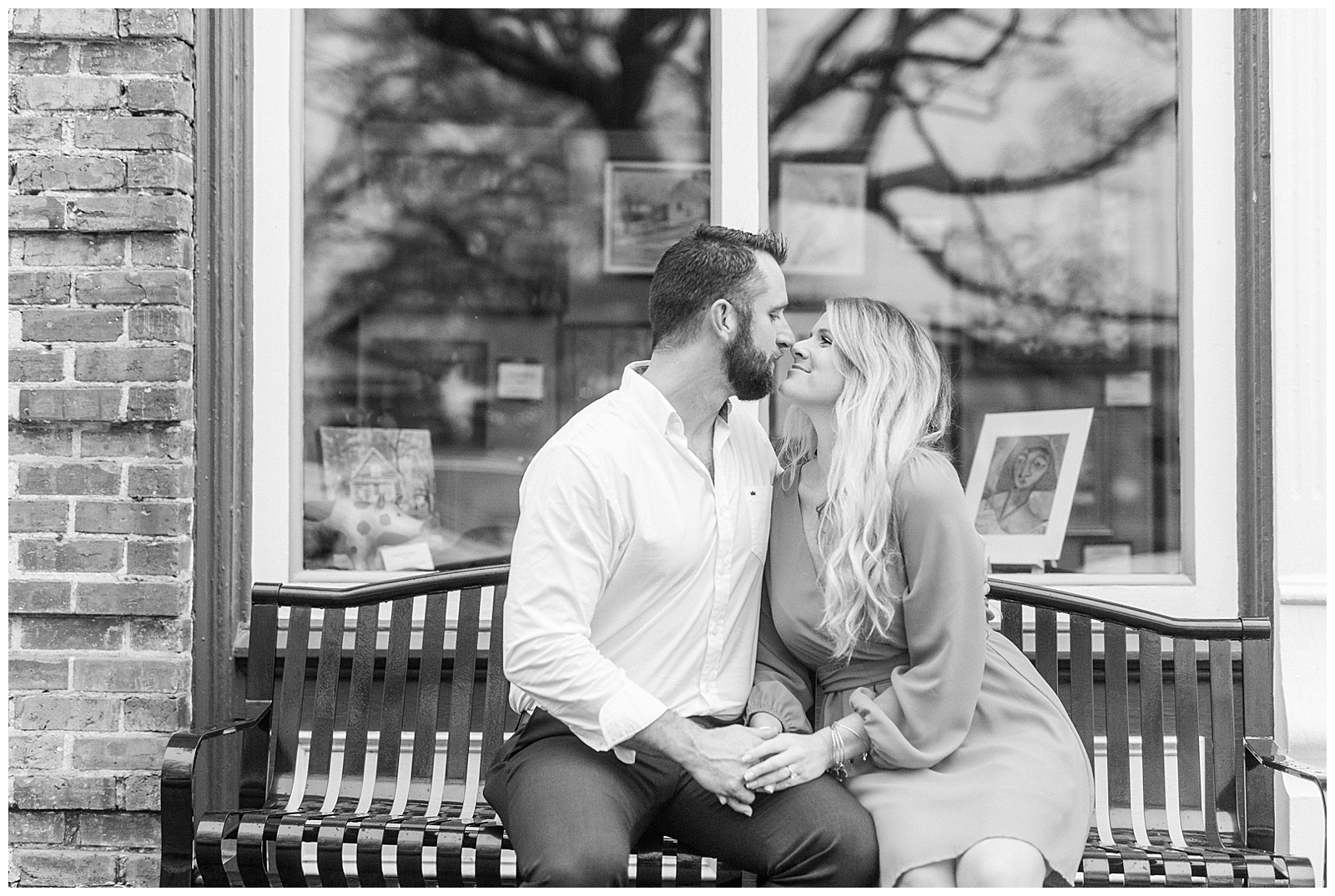 Adorable couple kissing on main street bench in front of downtown shop window in Waxhaw, NC Engagement Session with Bright Hot Pink Dress Outfit Ideas
