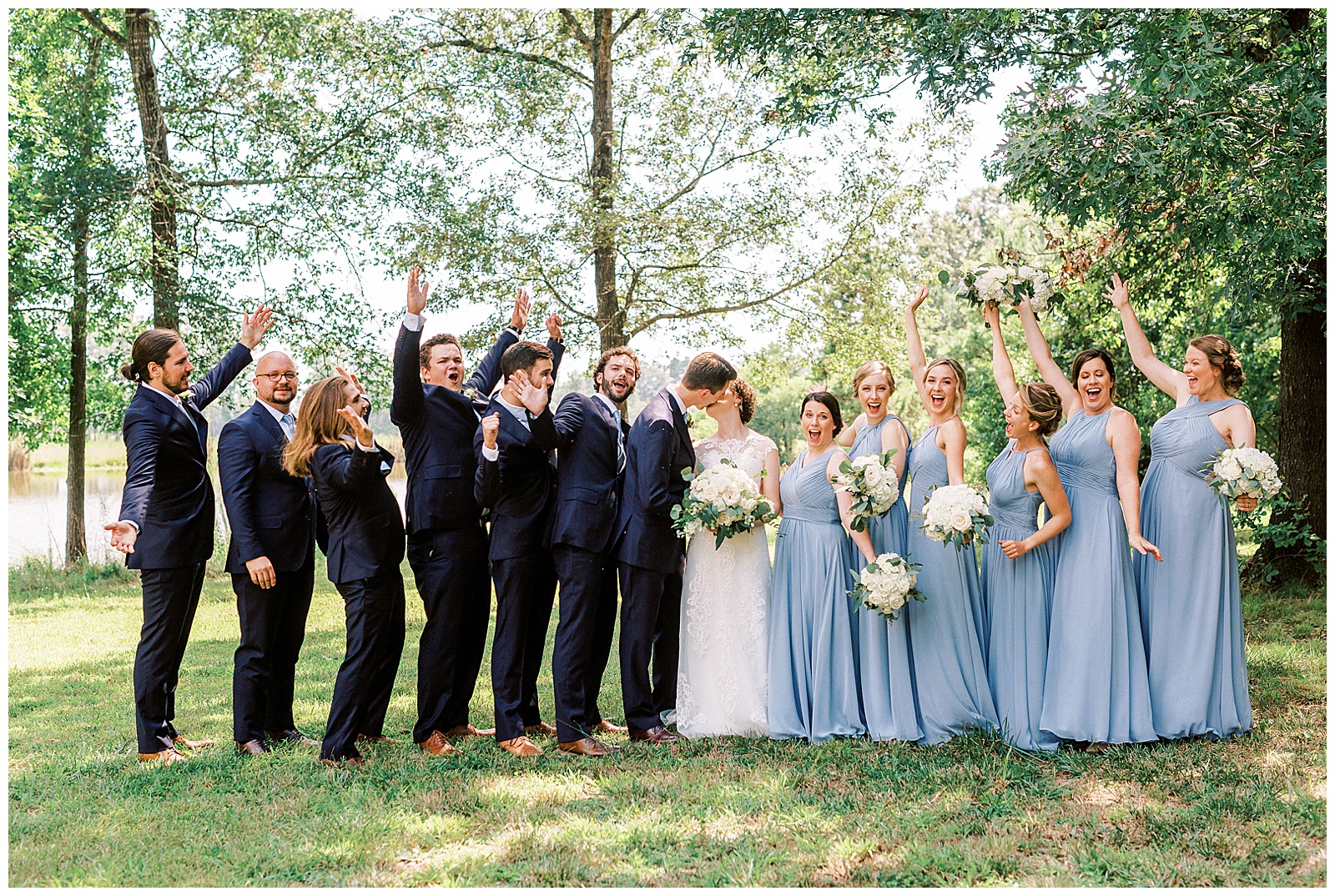 dusty blue bridesmaid bride tribe with white flower bouquet and navy blue suit groomsmen summer outdoor bridal party group portrait