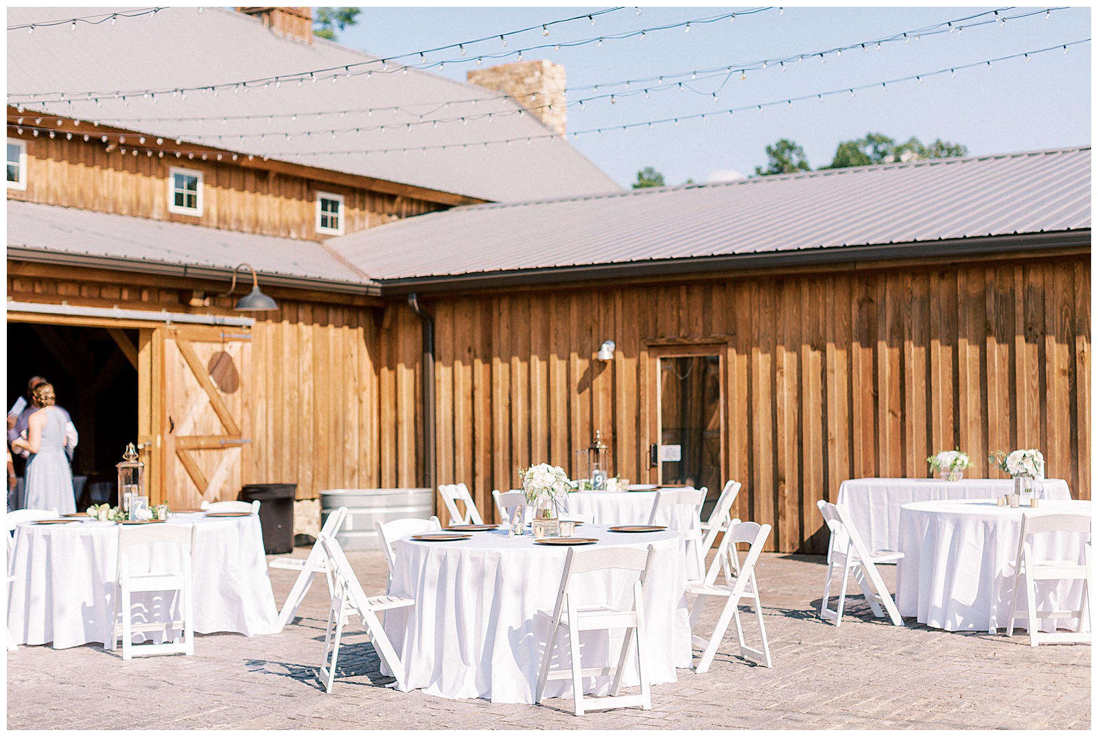 the farmstead huge wooden barn wedding venue doors side view with white tables set up outside