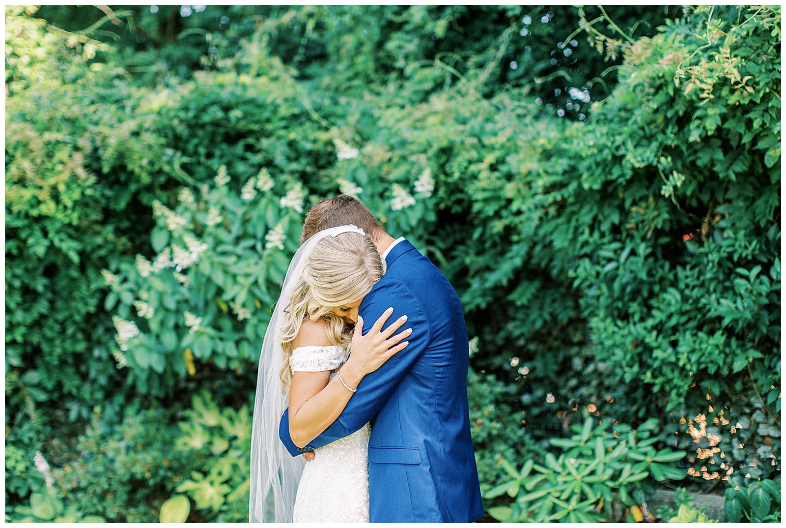 royal blue suited groom and blonde haired bride emotional first look outdoor in garden