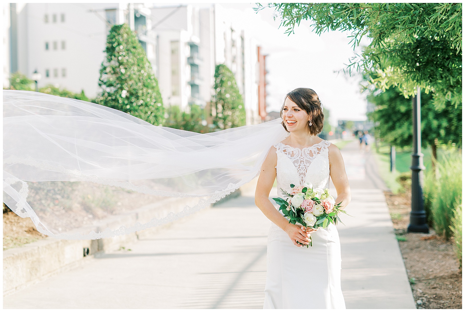 outdoor summer bridal portraits of short brown haired bride in lace dress with long train and long veil blowing in the wind