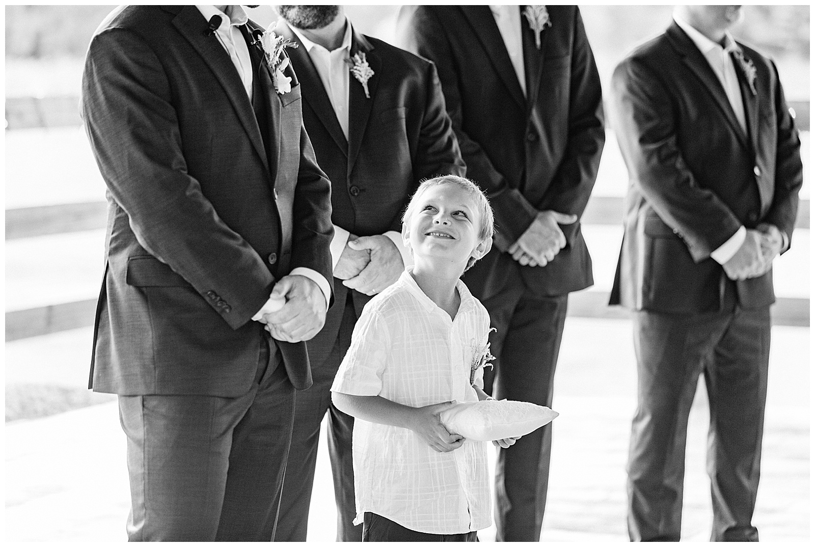 son of groom looks up at his dad while bride walks in black and white portrait