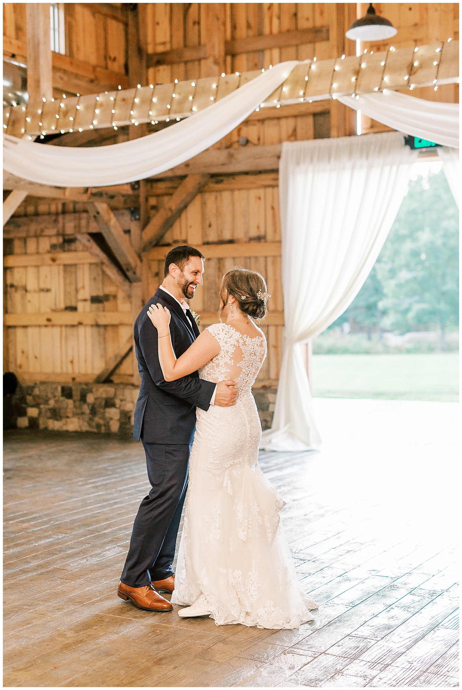 bride and groom first dance at indoor summer wedding reception in wooden barn