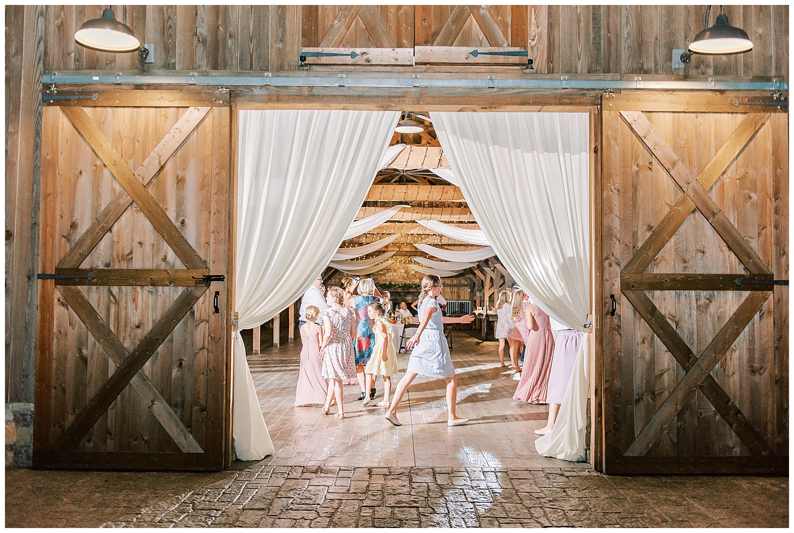 guests dance at indoor summer wedding reception in wooden barn