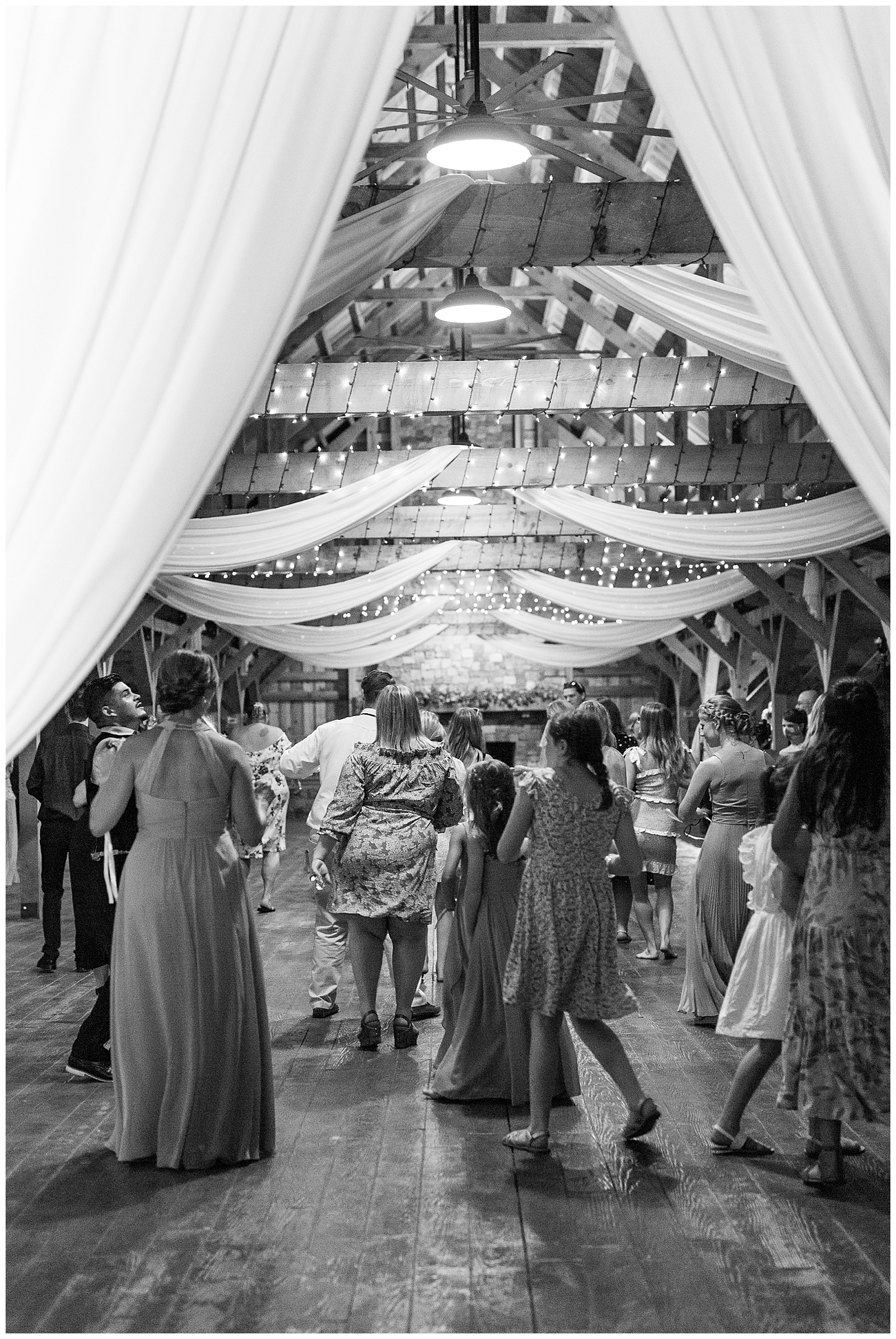 guests dance at indoor summer wedding reception in wooden barn