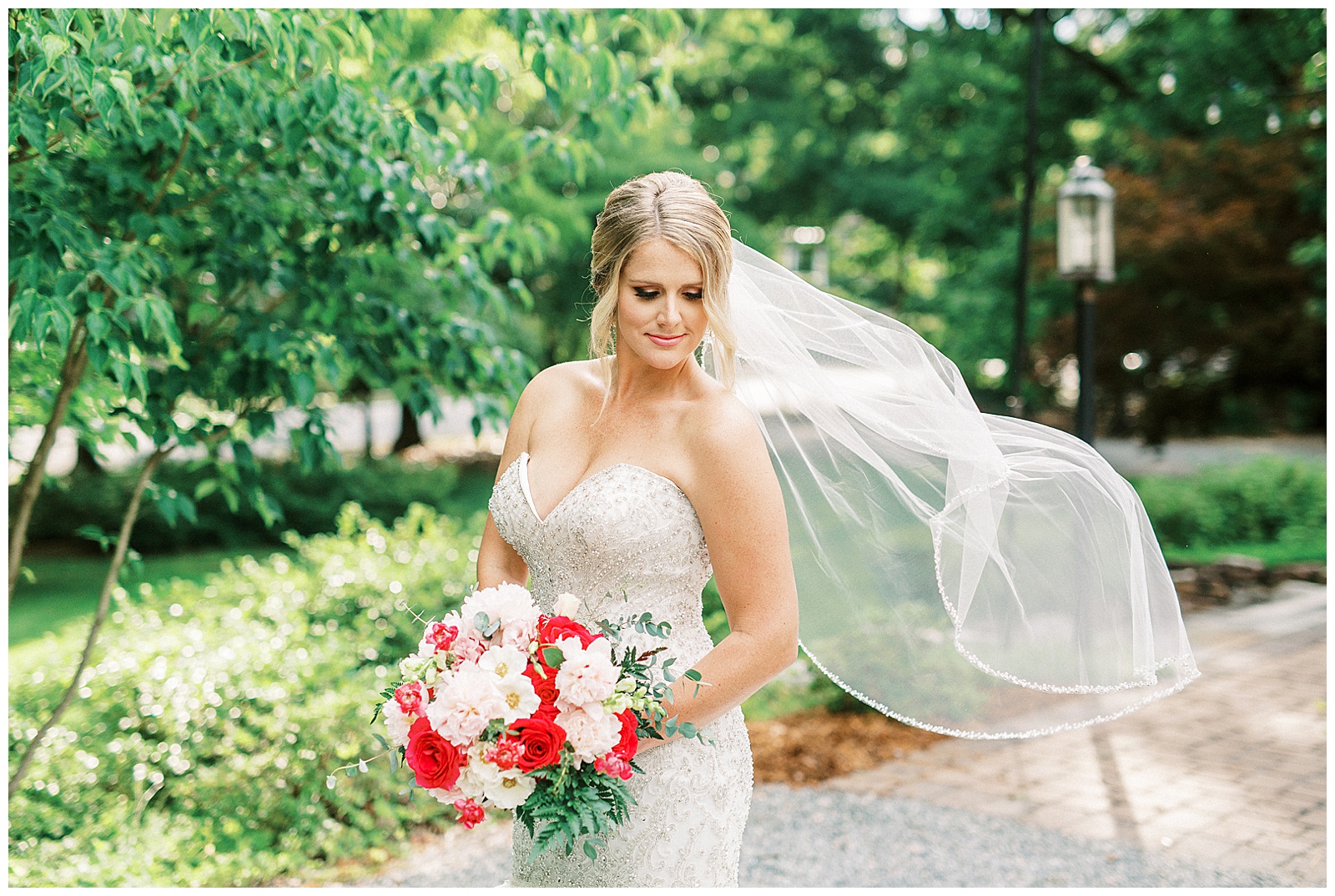 veil shots of gorgeous blonde haired bride with mermaid dress and fluffy tulle skirt and white and red bouquet in outdoor bridal portraits