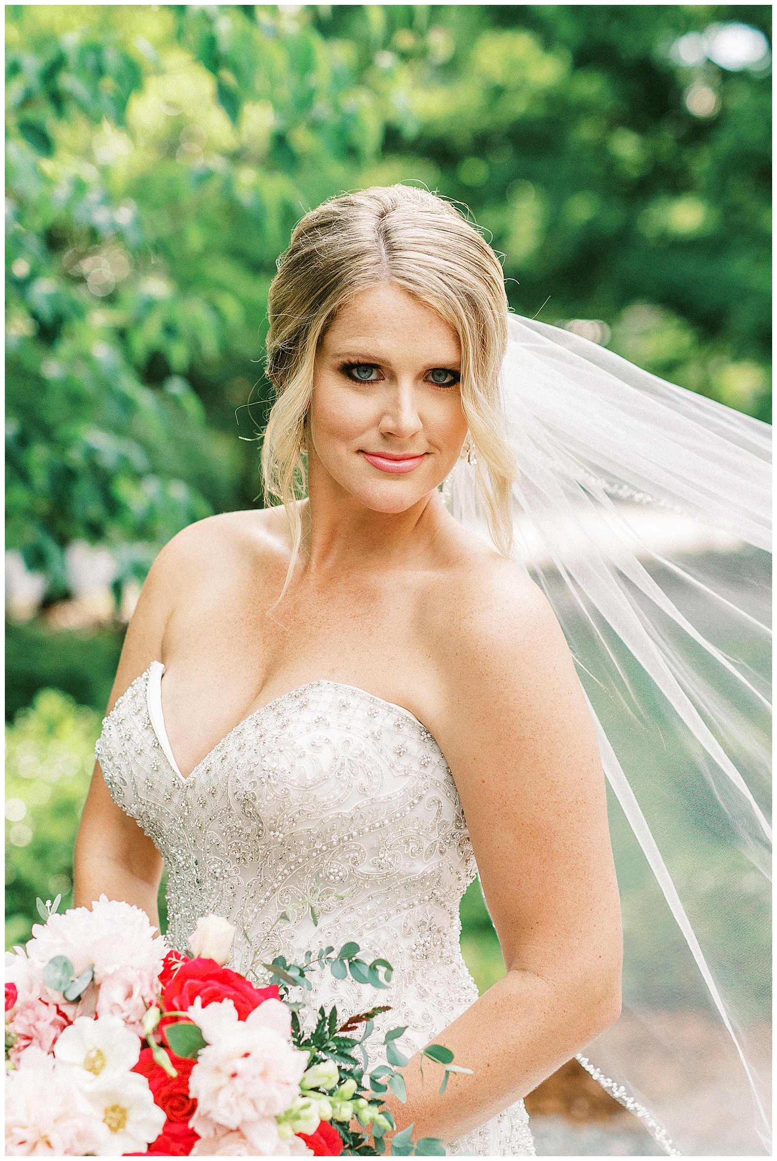 veil shots of gorgeous blonde haired bride with mermaid dress and fluffy tulle skirt and white and red bouquet in outdoor bridal portraits
