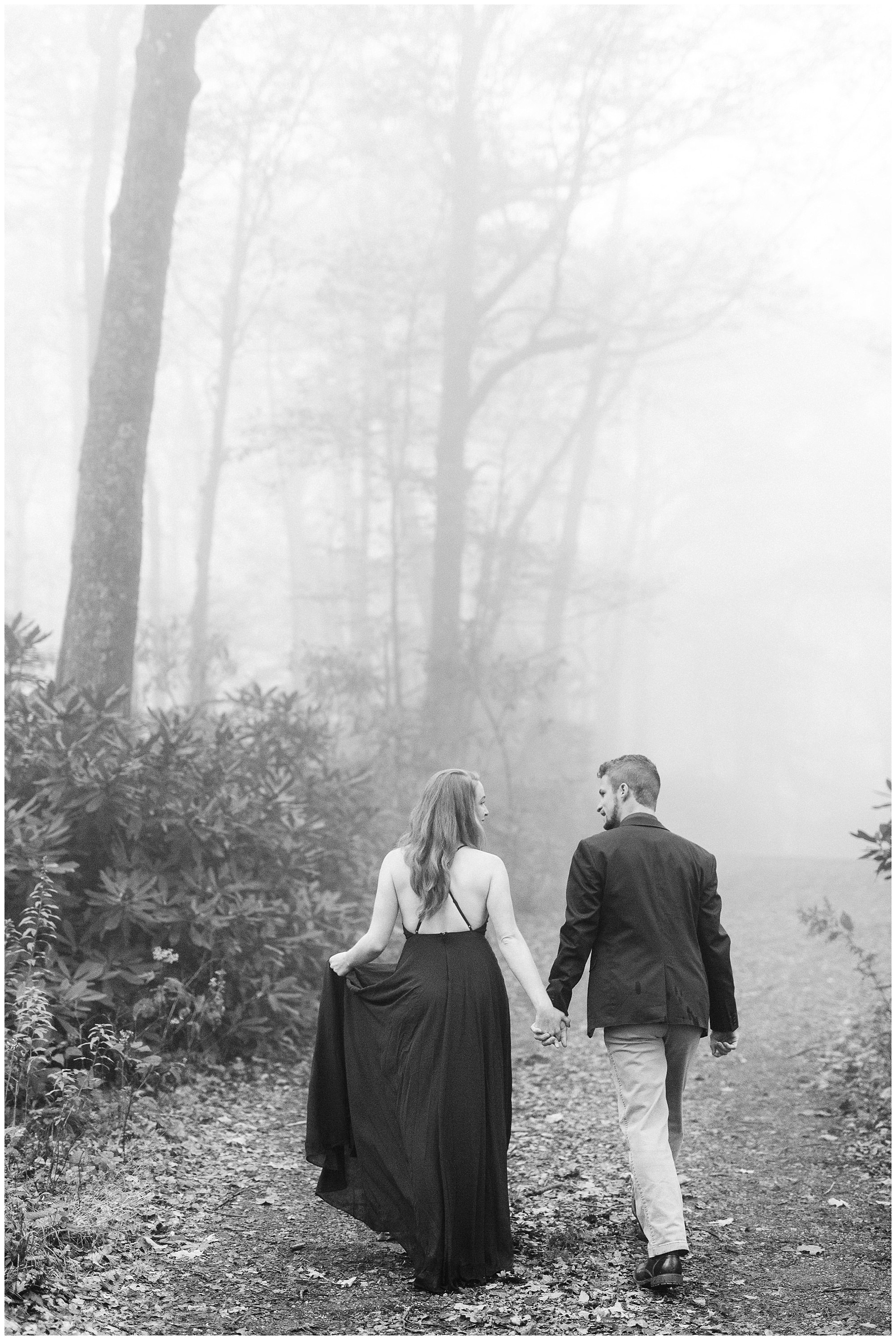 couple walks through path at Moses Cone Manor during dramatic foggy mountain engagement session