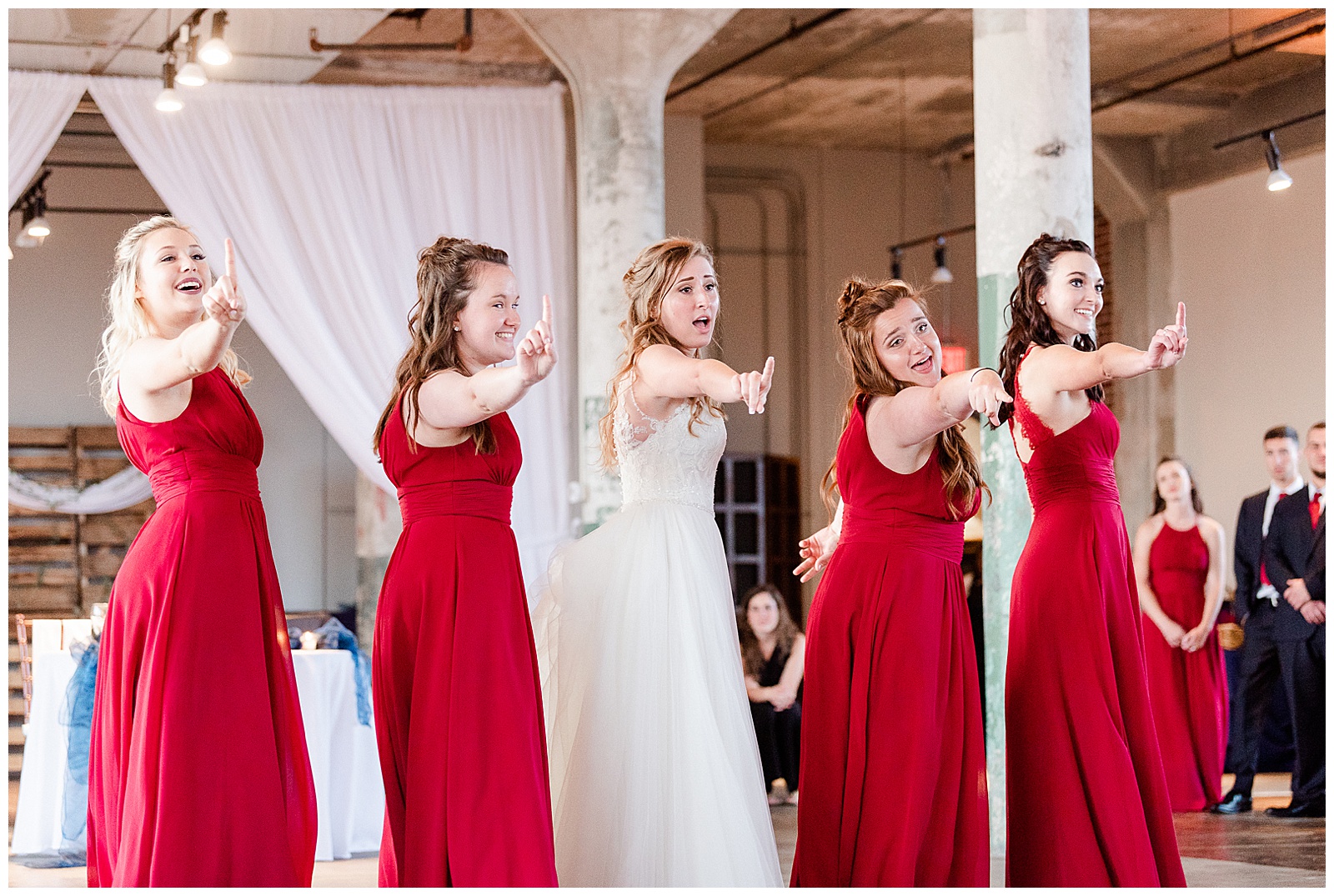 Bride Surprises Groom with Bridesmaid Dance at Rustic Airy Indoor Wedding Venue with fairy lights - Red-Themed Bridesmaid Dress Ideas from Elegant Modern Summer Wedding in Charlotte, NC | check out the full wedding at KevynDixonPhoto.com