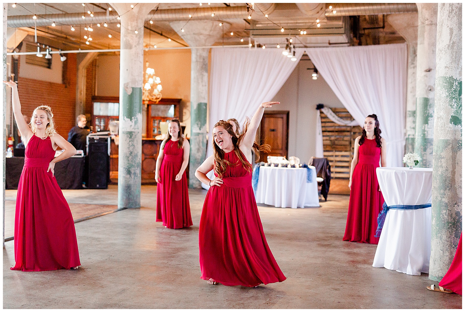 Bride Surprises Groom with Bridesmaid Dance at Rustic Airy Indoor Wedding Venue with fairy lights - Red-Themed Bridesmaid Dress Ideas from Elegant Modern Summer Wedding in Charlotte, NC | check out the full wedding at KevynDixonPhoto.com