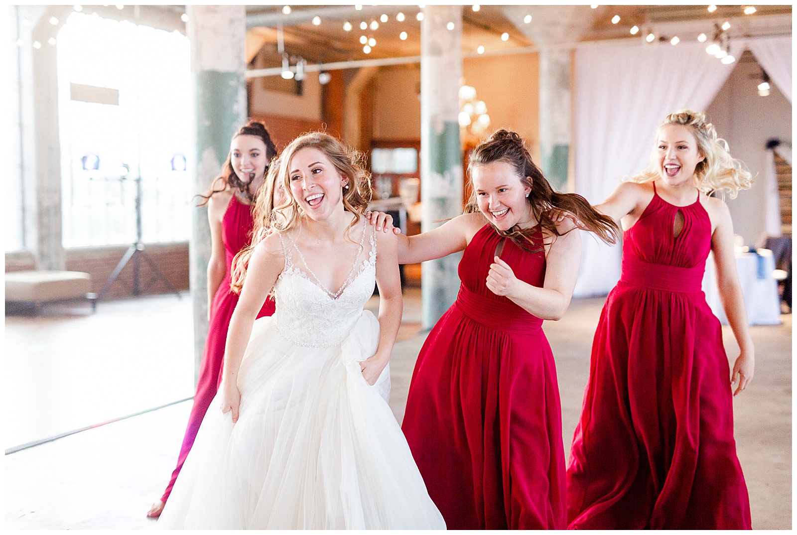 Bride Surprises Groom with Bridesmaid Dance at Rustic Airy Indoor Wedding Venue with fairy lights - Red-Themed Bridesmaid Dress Ideas from Elegant Modern Summer Wedding in Charlotte, NC | check out the full wedding at KevynDixonPhoto.com