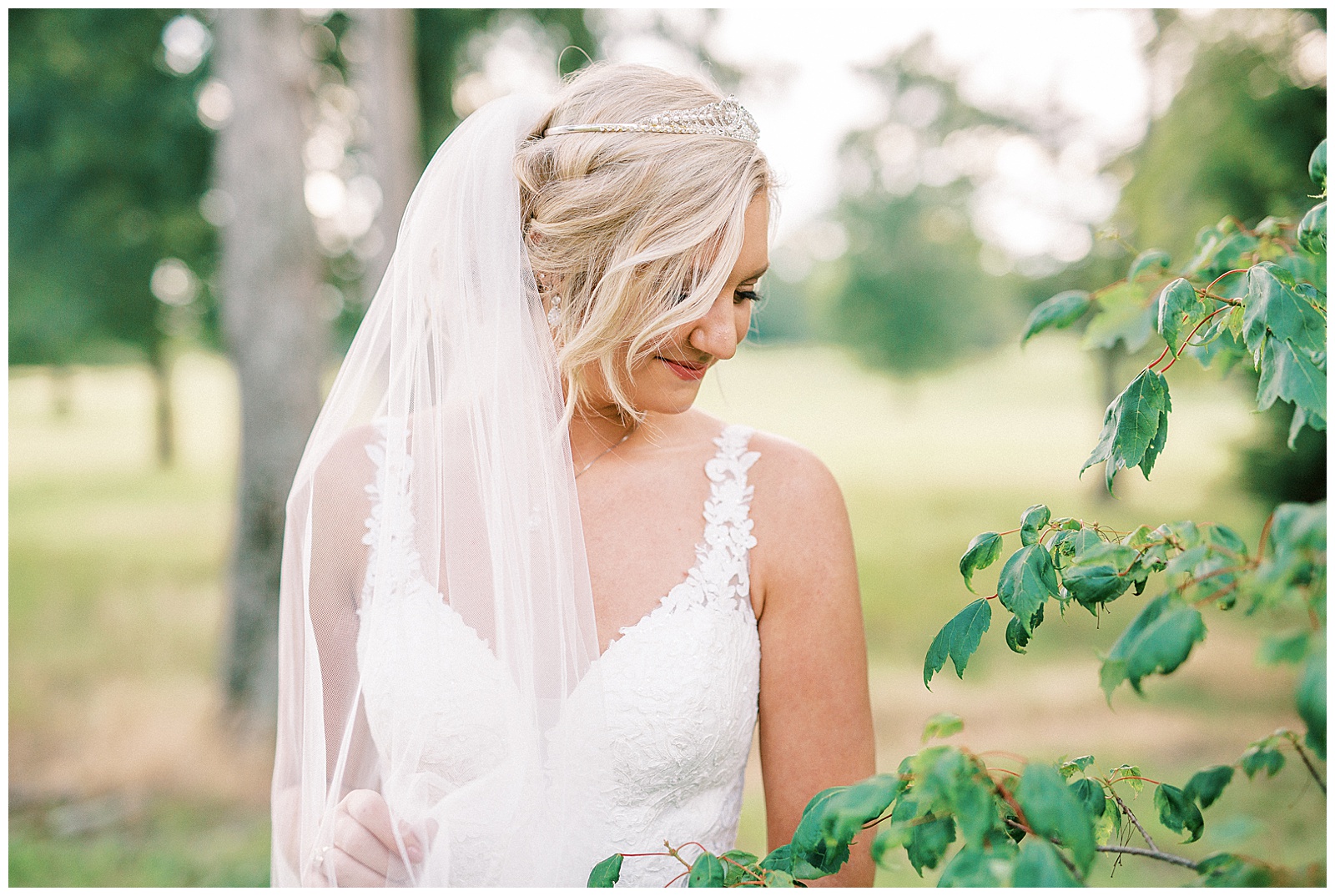 long veil white lace dress blonde haired updo bride poses in Summer Forest Outdoor Bridal Session