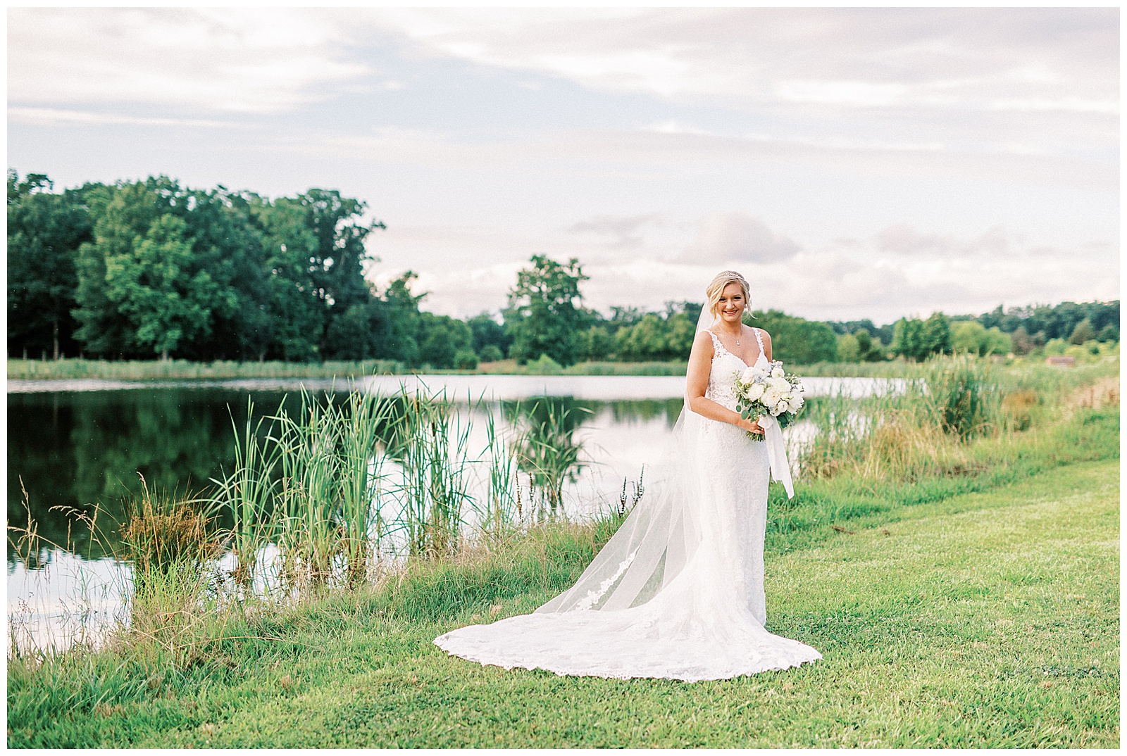 white lace dress blonde haired updo bride poses in front of summer lake Outdoor Bridal Session
