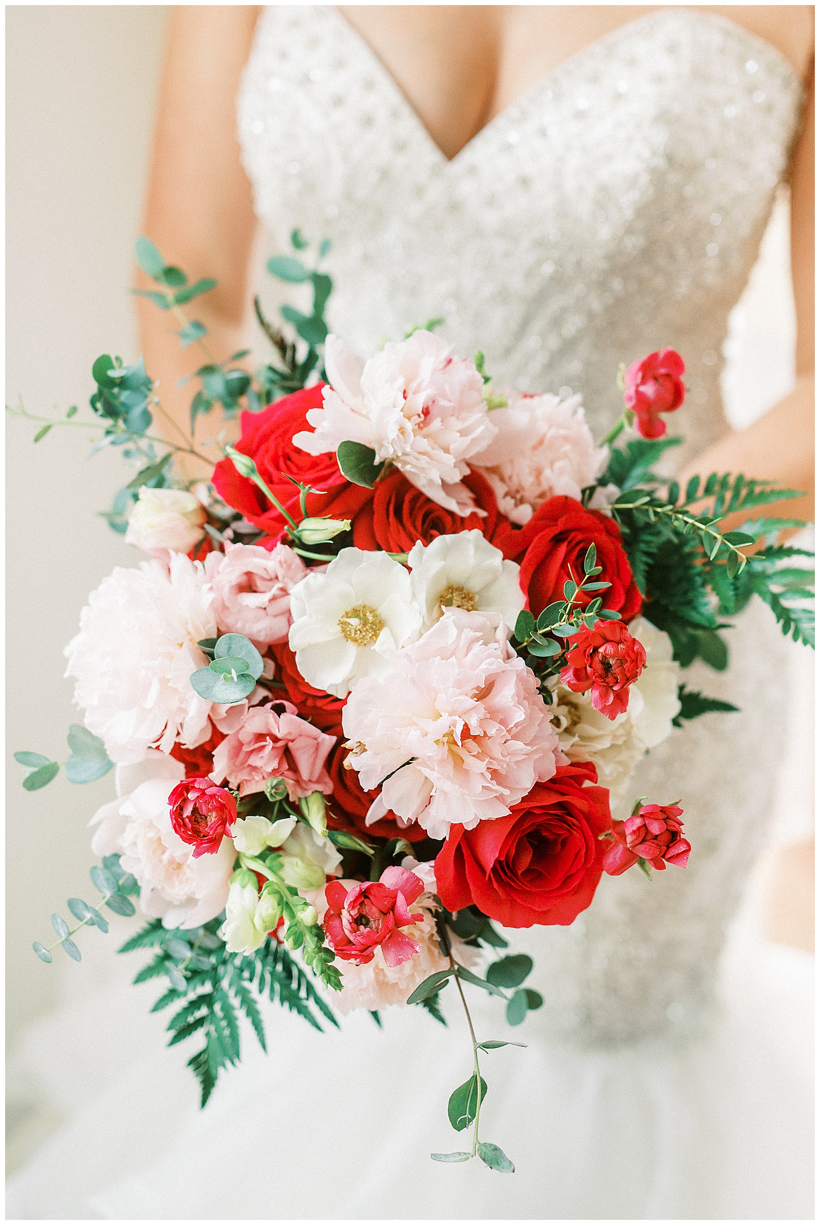 gorgeous light and airy indoor bridal portraits of blonde haired bride in mermaid dress with loads of tulle next to floor length window with red and white bouquet