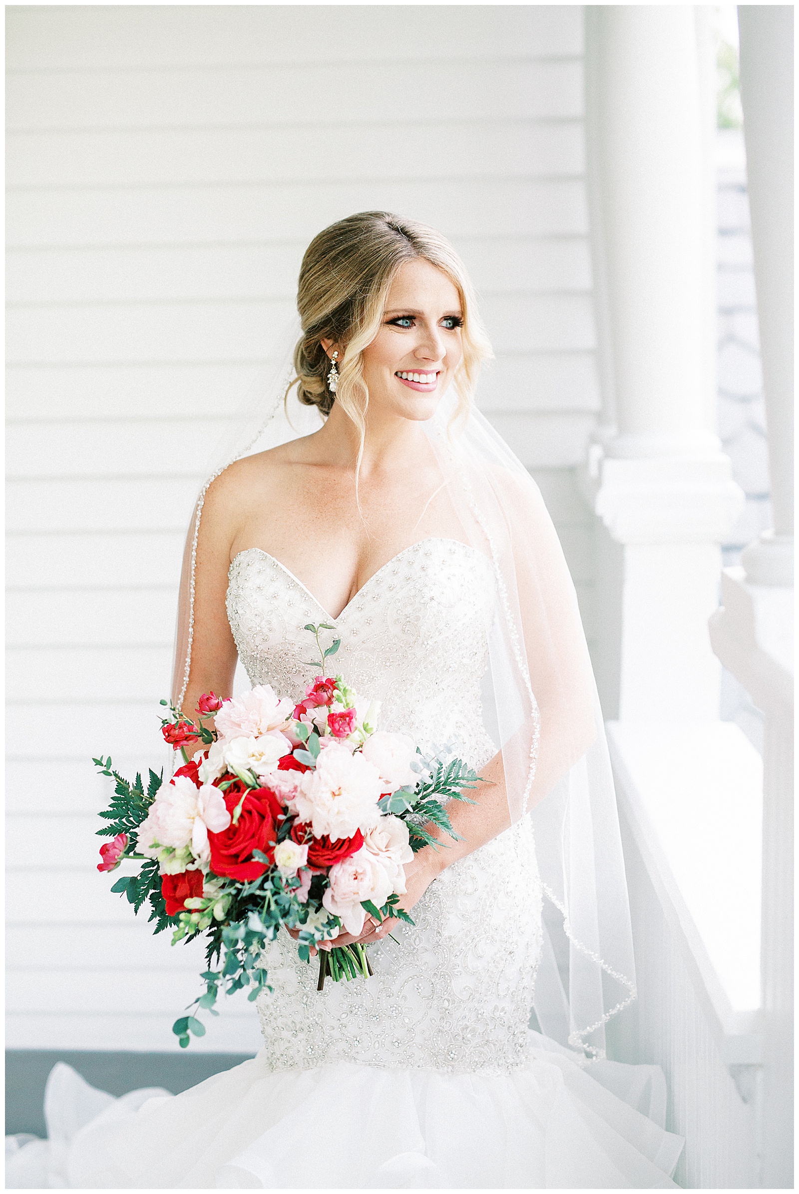 gorgeous light and airy outdoor bridal portraits of blonde haired bride in mermaid dress with loads of tulle on southern porch with red and white bouquet