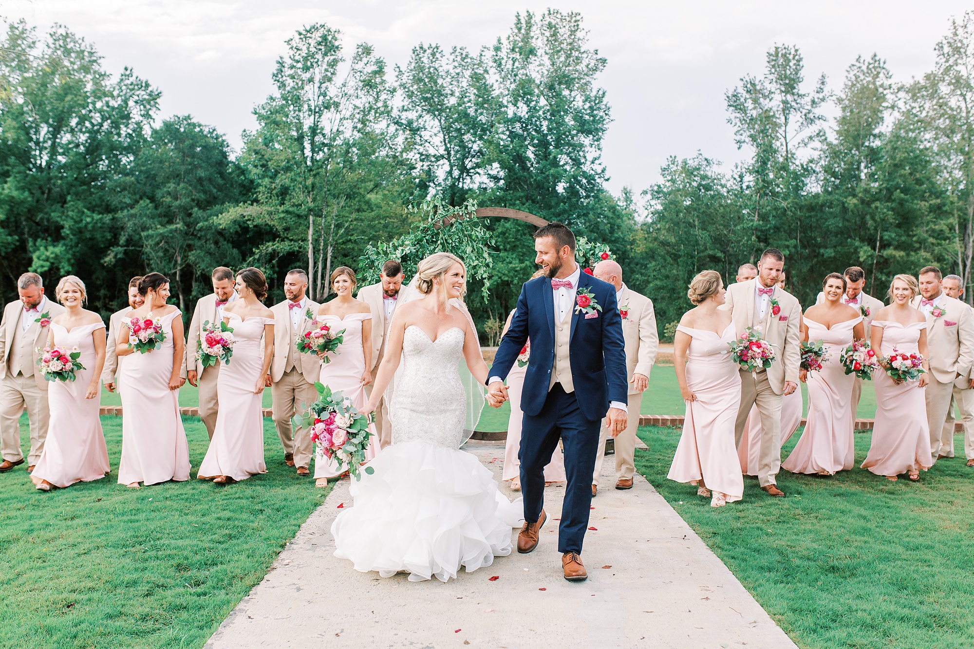 bride and groom hold hands waking in front of bridal party