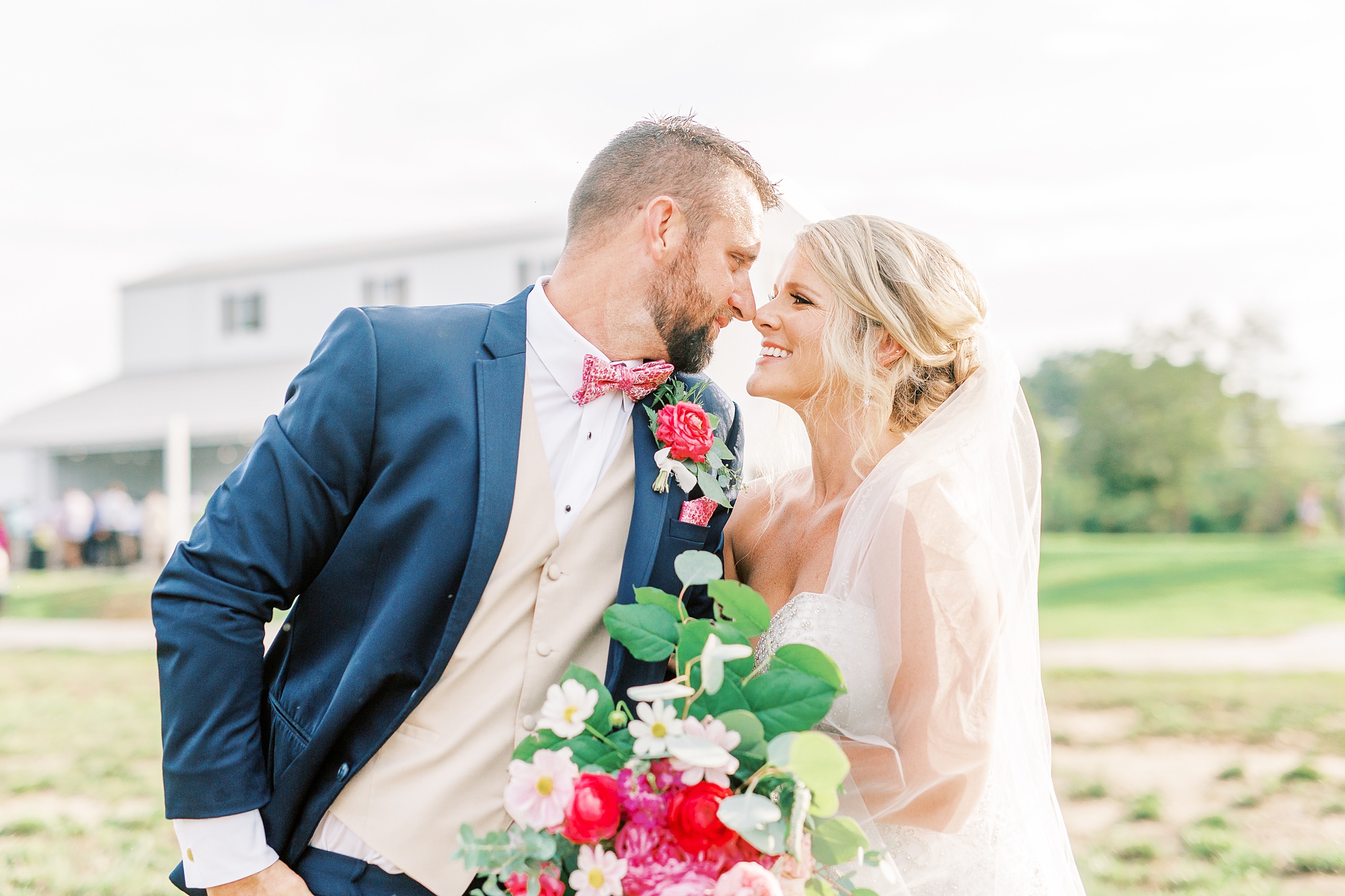 bride and groom stand nose to nose laughing in front of Belle's Venue