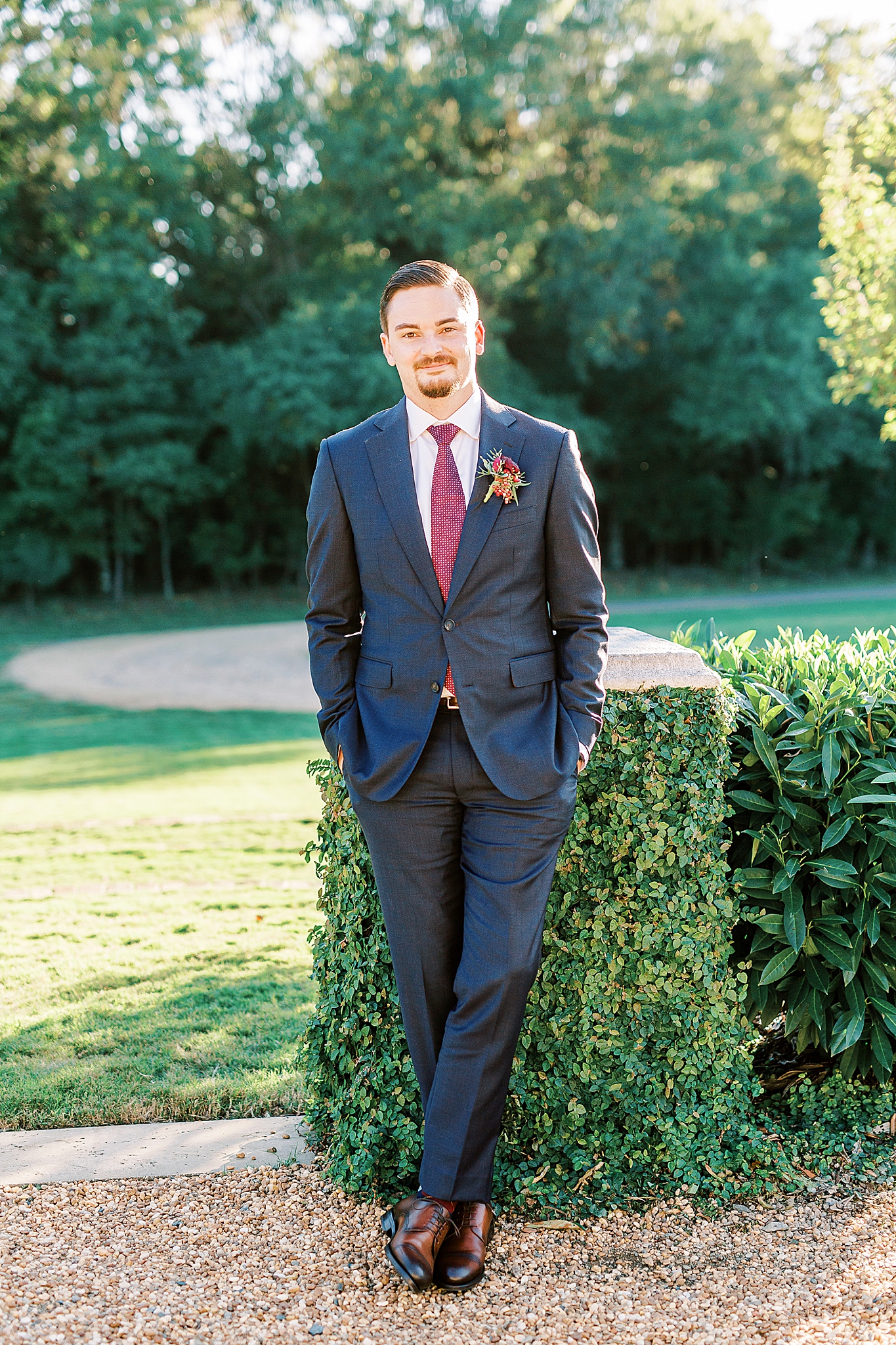 groom poses by stone wall covered in ivy