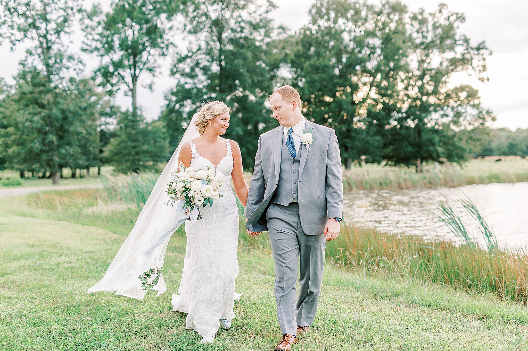 bride and groom hold hands walking along lake at The Farm at Brusharbor