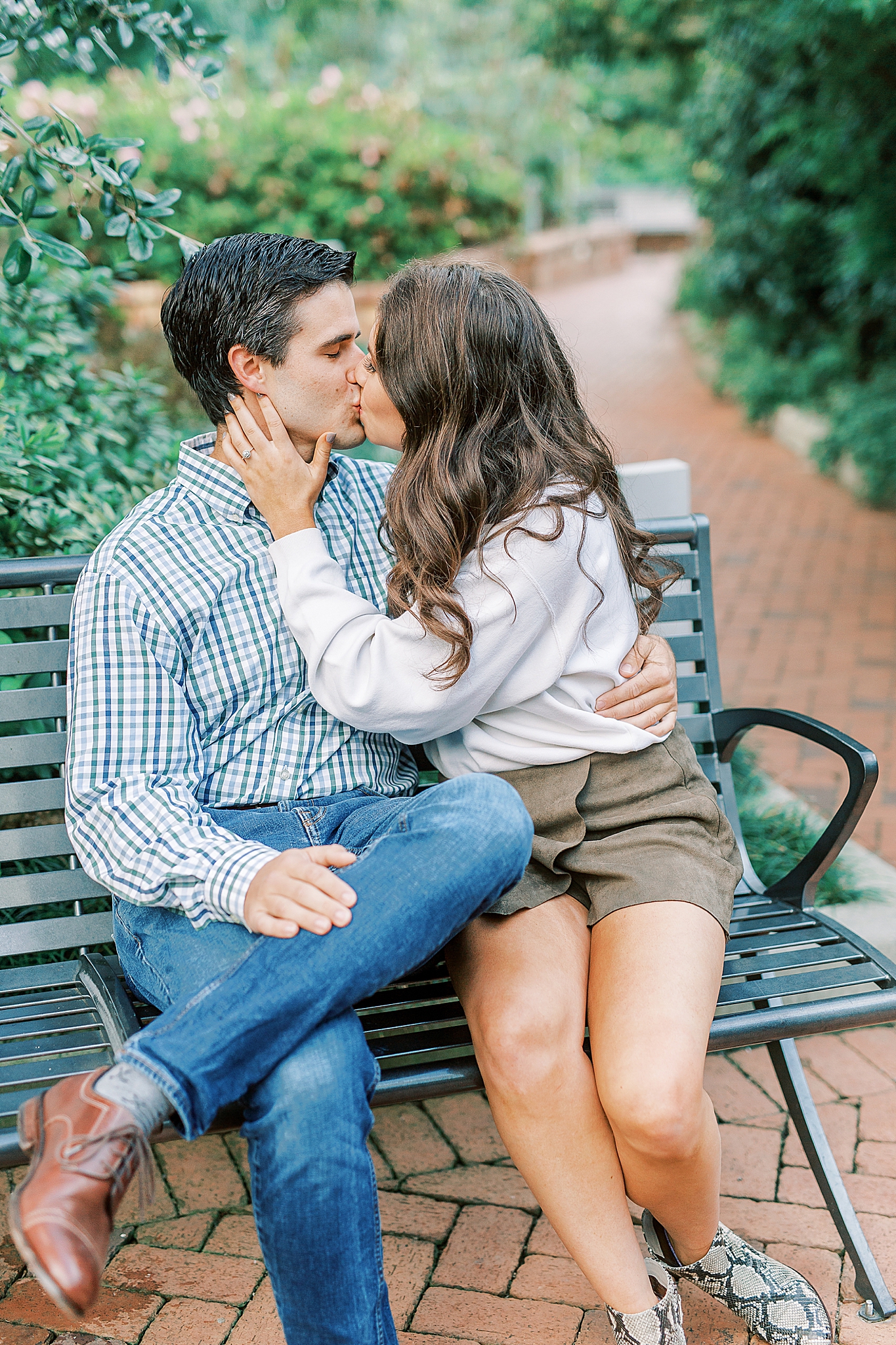 engaged couple kisses on park bench at Romare Bearden Park