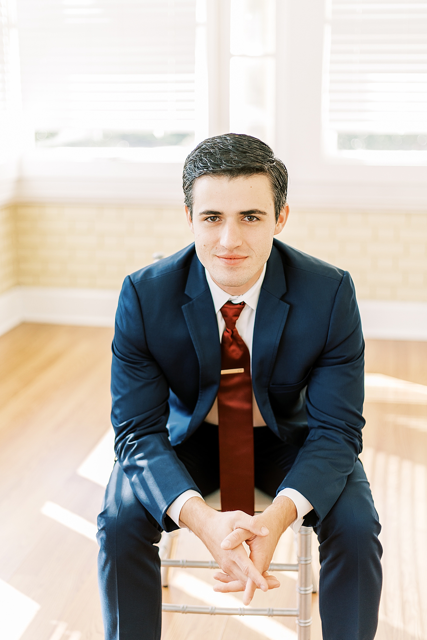 groom in navy suit sits in Separk Mansion
