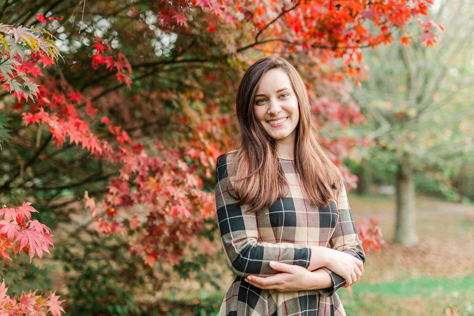 senior girl crosses arms by fall trees