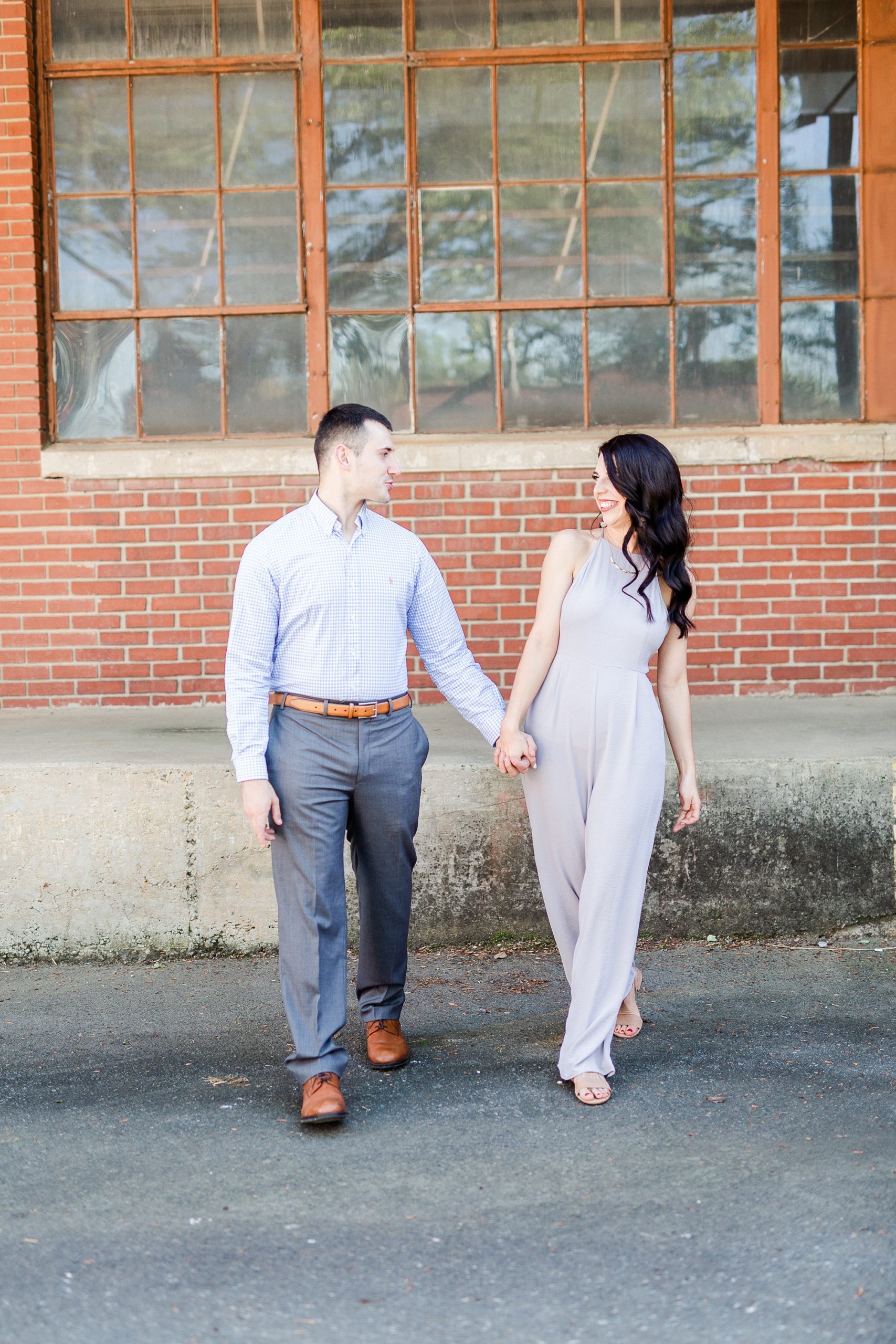 engaged couple holds hands walking through Camp North End