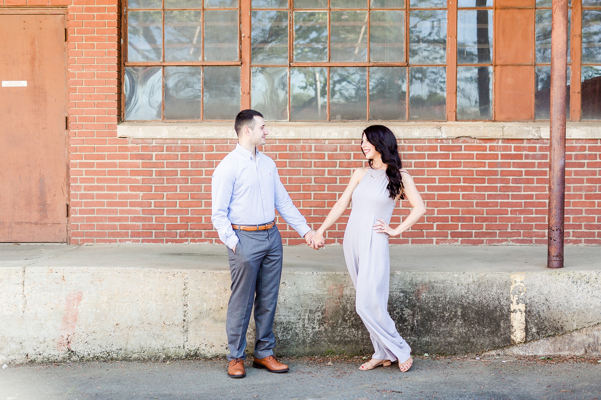 bride and groom hold hands posing in front of brick building