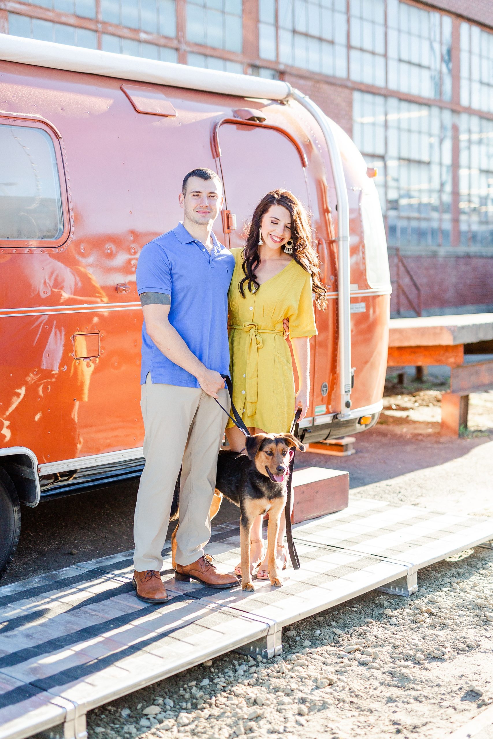 engaged couple poses with dog outside red airstream