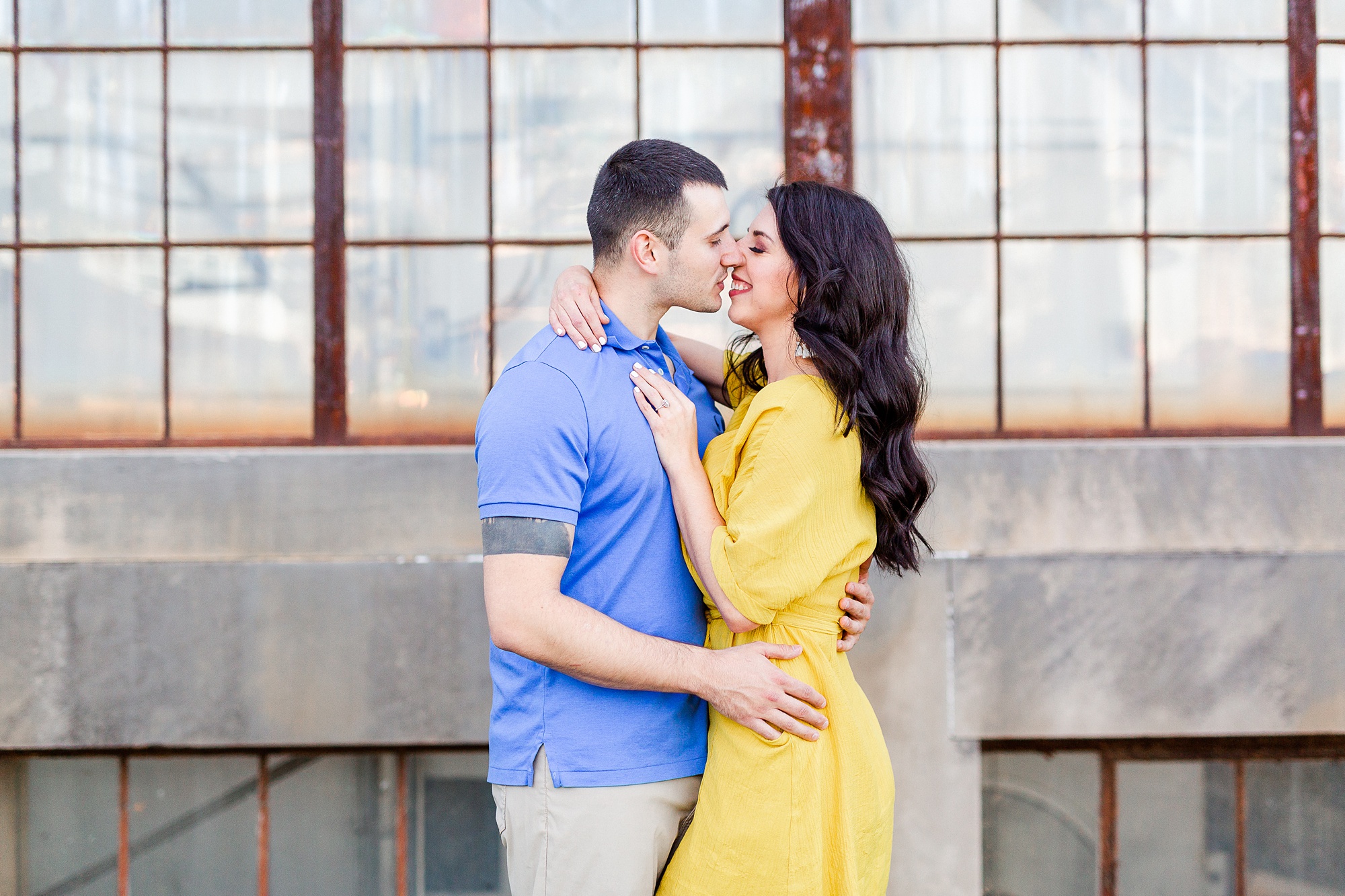engaged couple kisses outside window of old factory