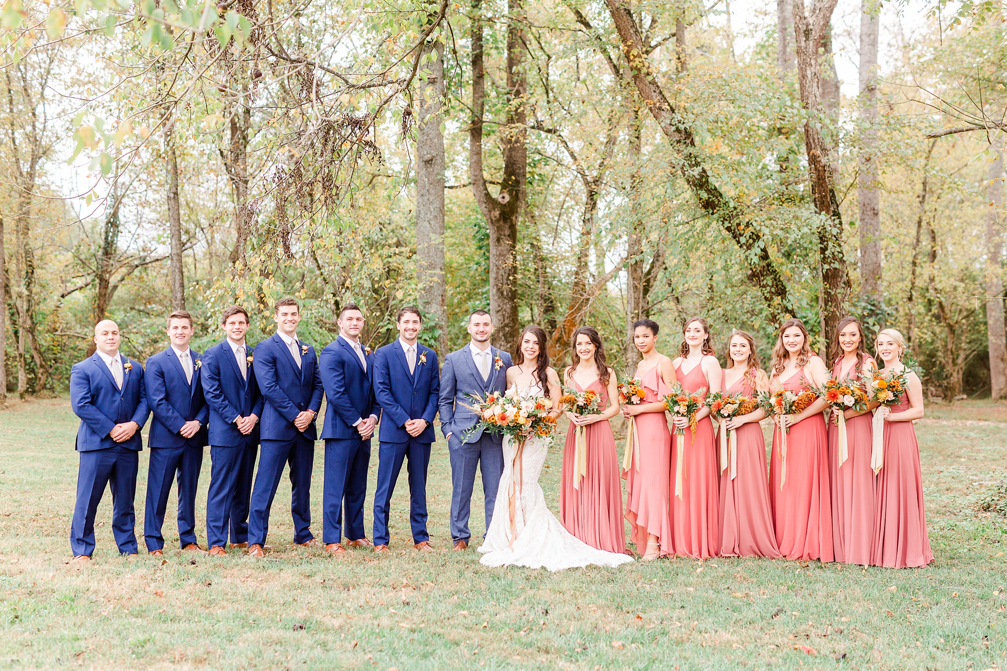 bride and groom pose with bridal party in coral and navy