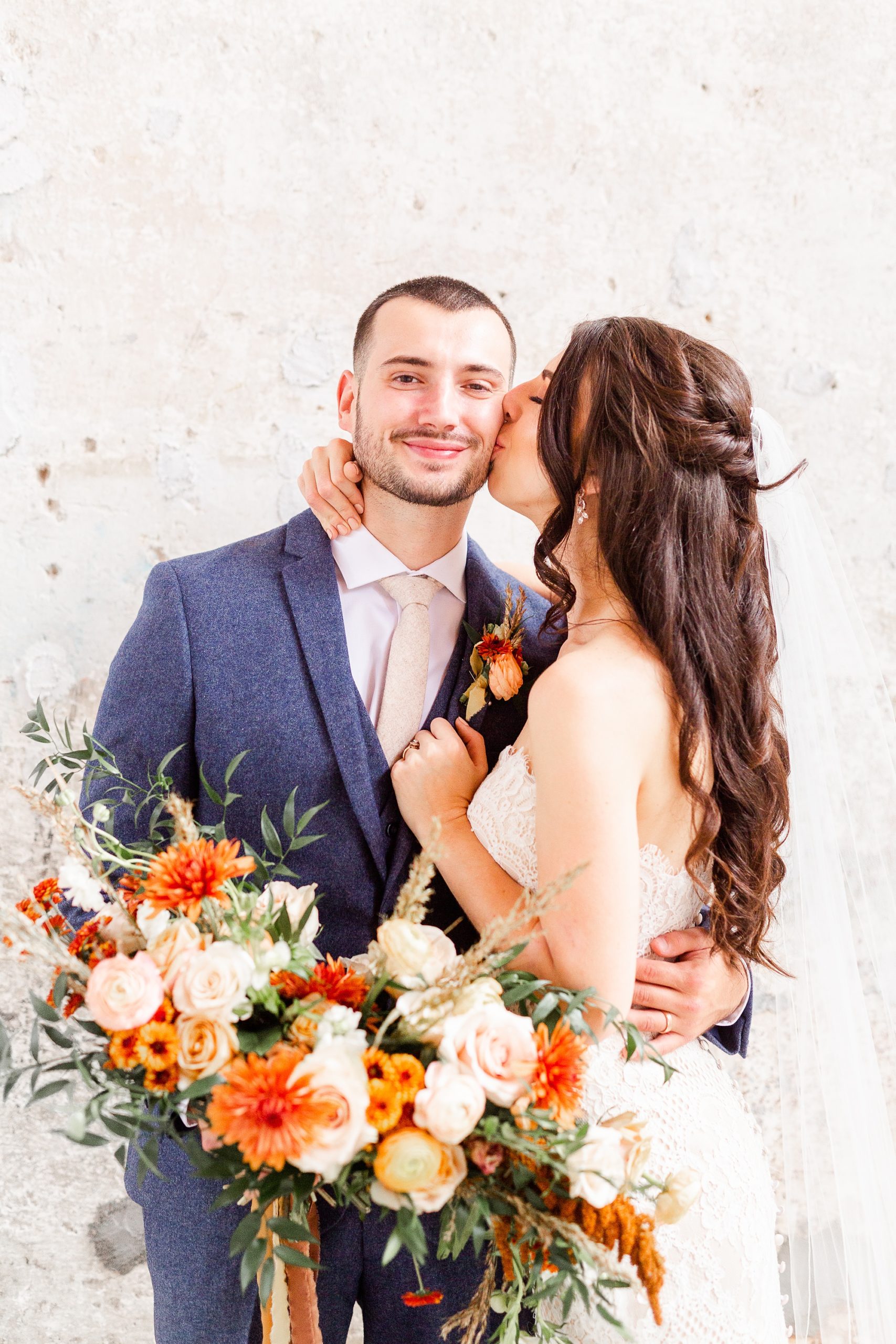 bride kisses groom on the cheek in front of brick wall at Providence Cotton Mill