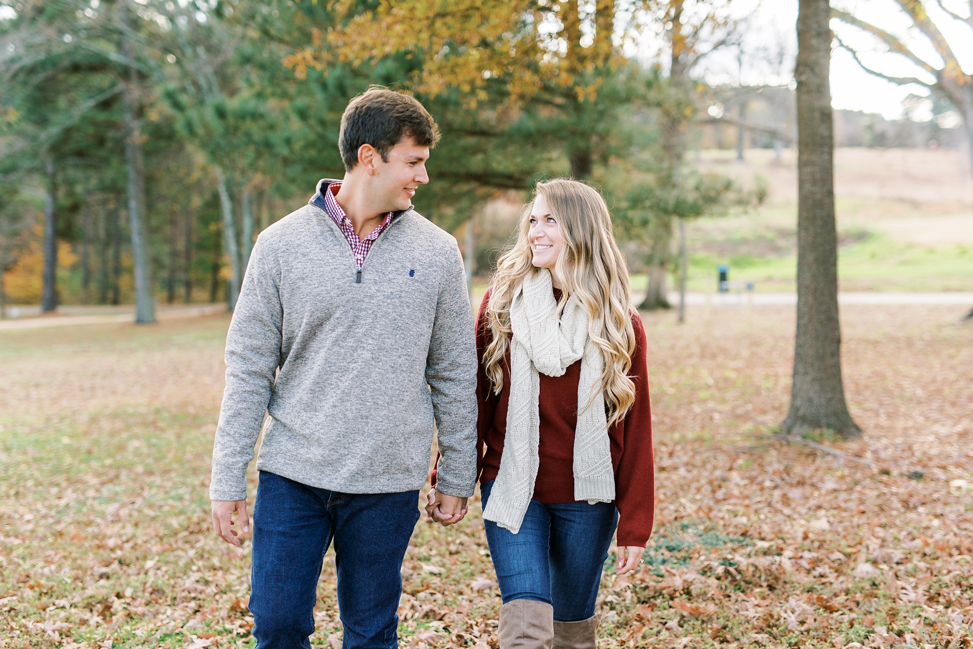 engaged couple walks through fallen leaves outside NC Museum of Art