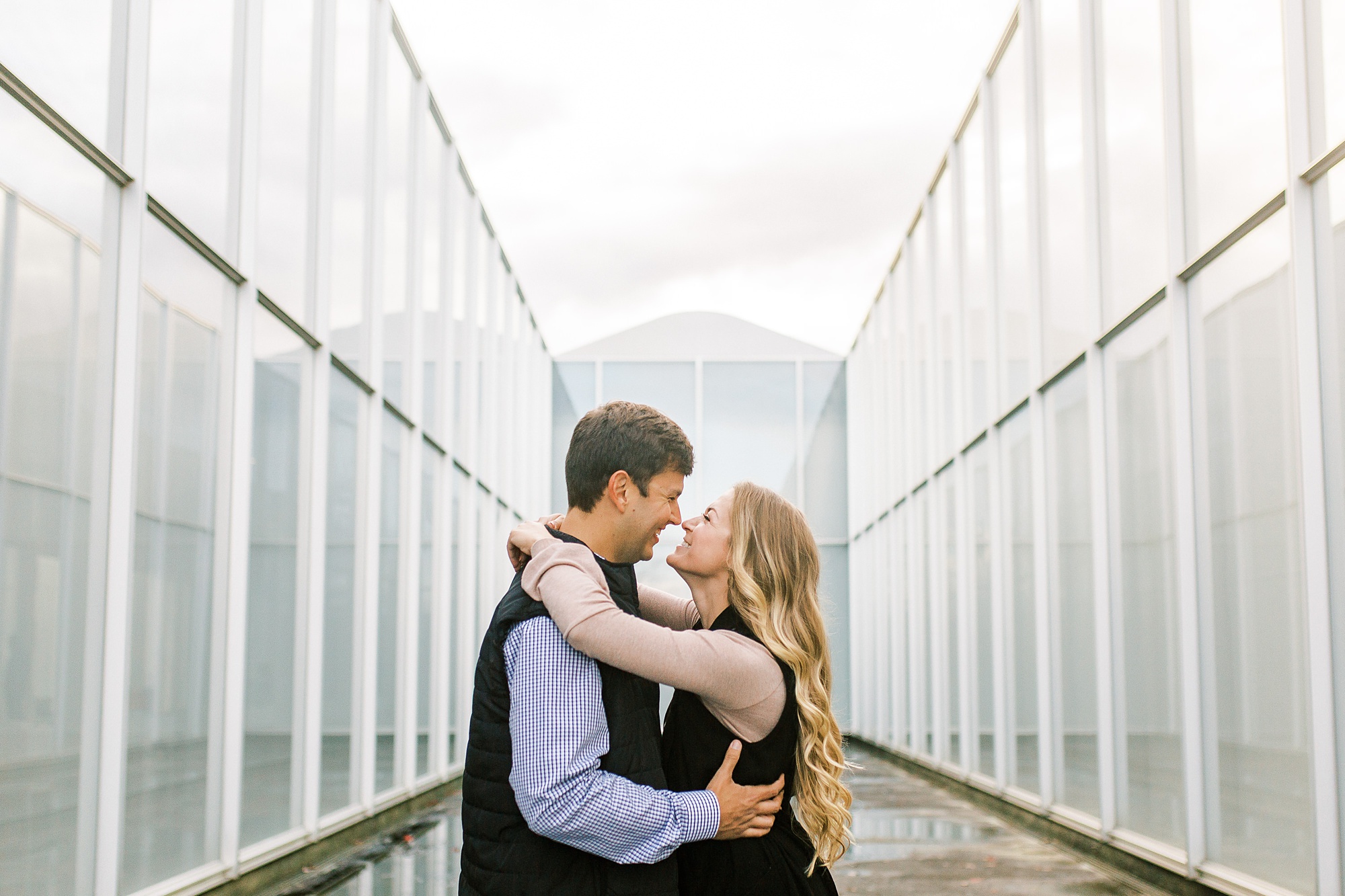 engaged couple poses in between glass buildings at NC Museum of Art