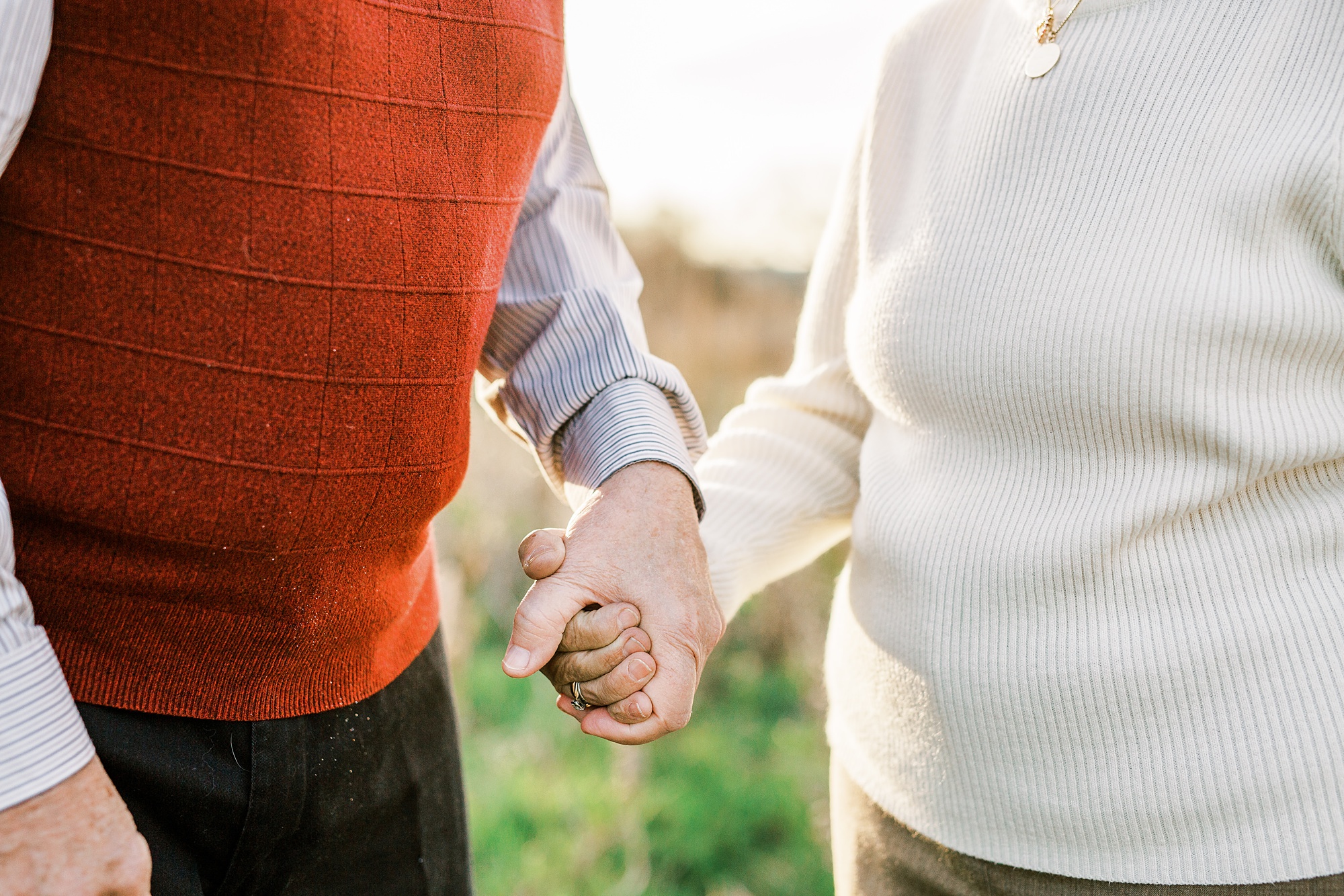 married couple holds hands walking through field