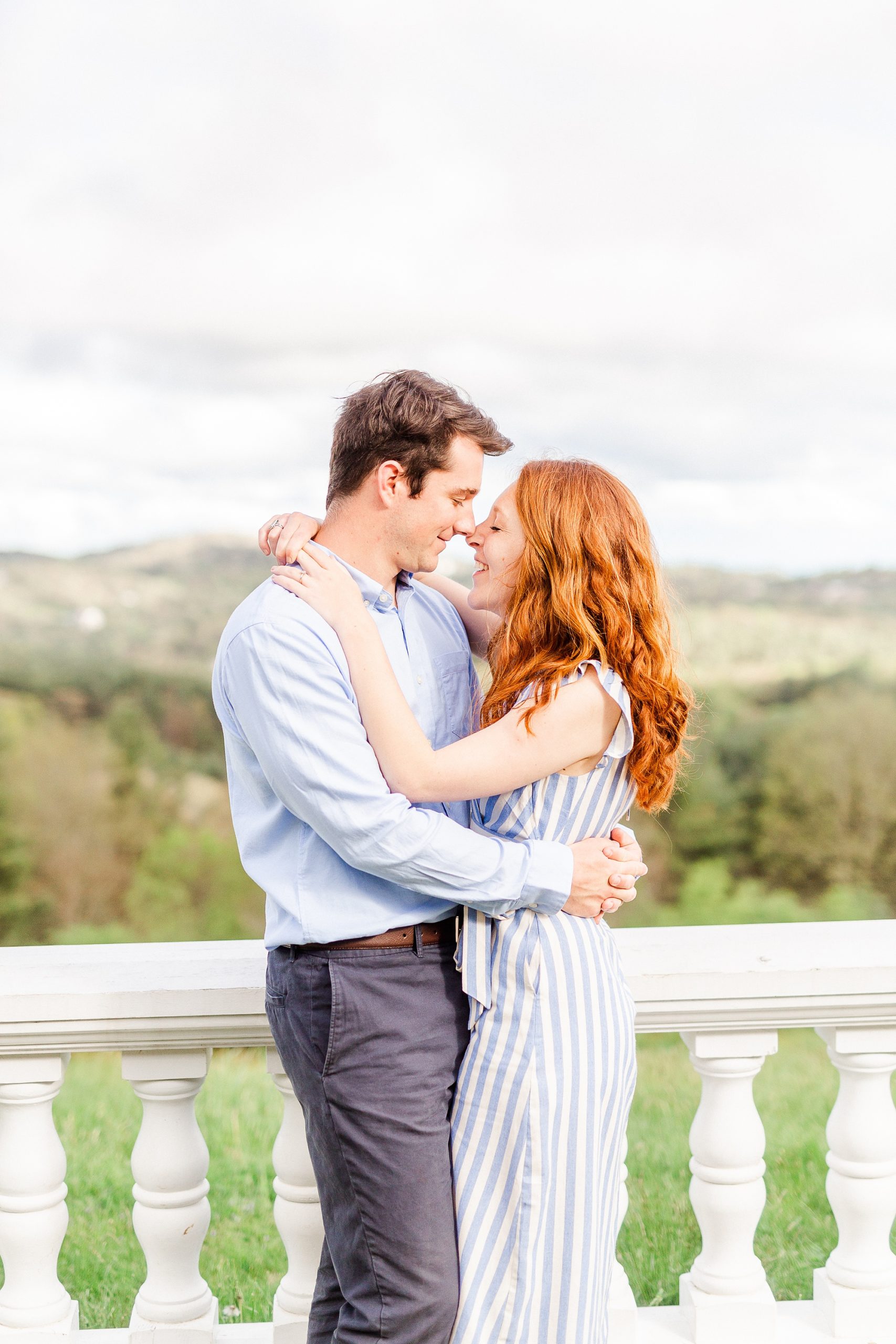 engaged couple stands touching noses on balcony of Moses Cone Manor