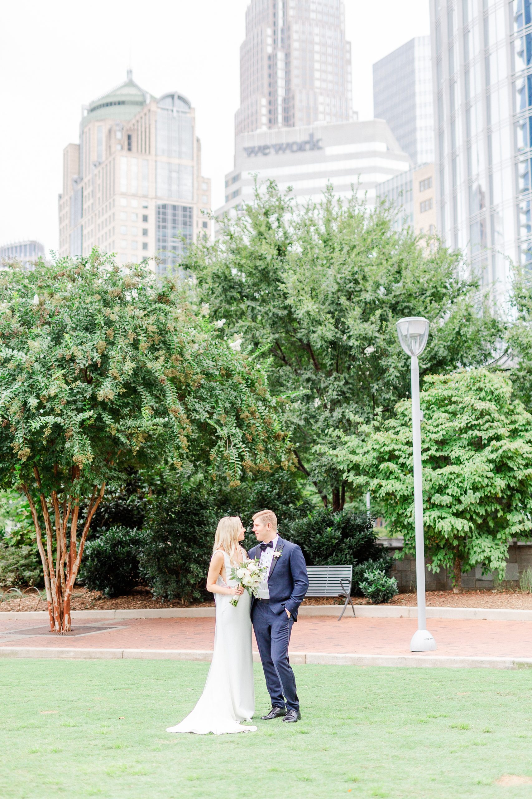 bride and groom pose in front of Charlotte skyline