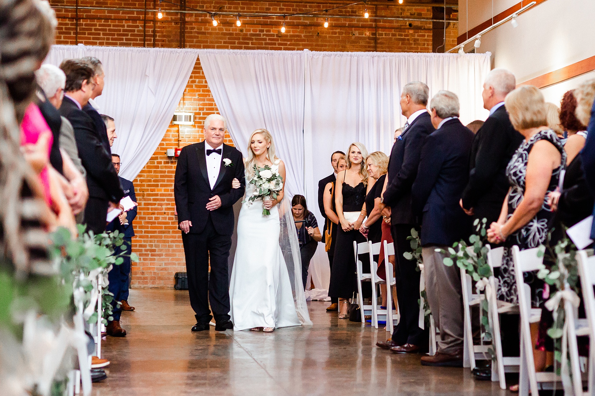 bride walks down aisle with father at Design Center Atrium