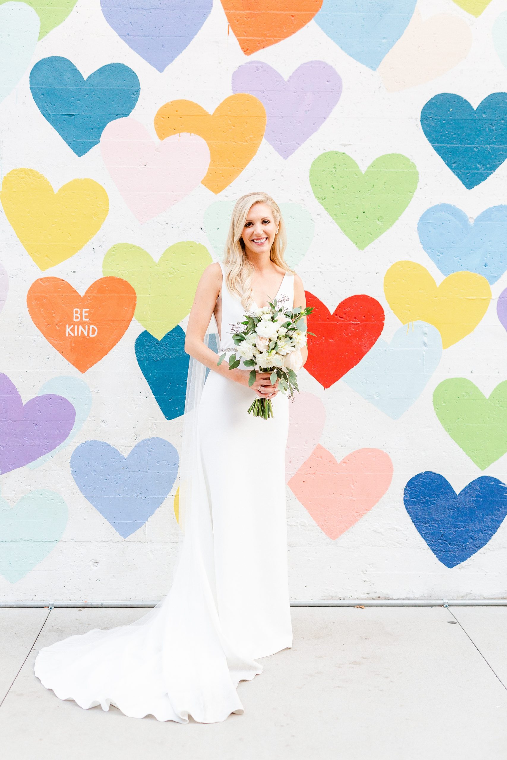 bride holds bouquet of white flowers by colorful mural of hearts