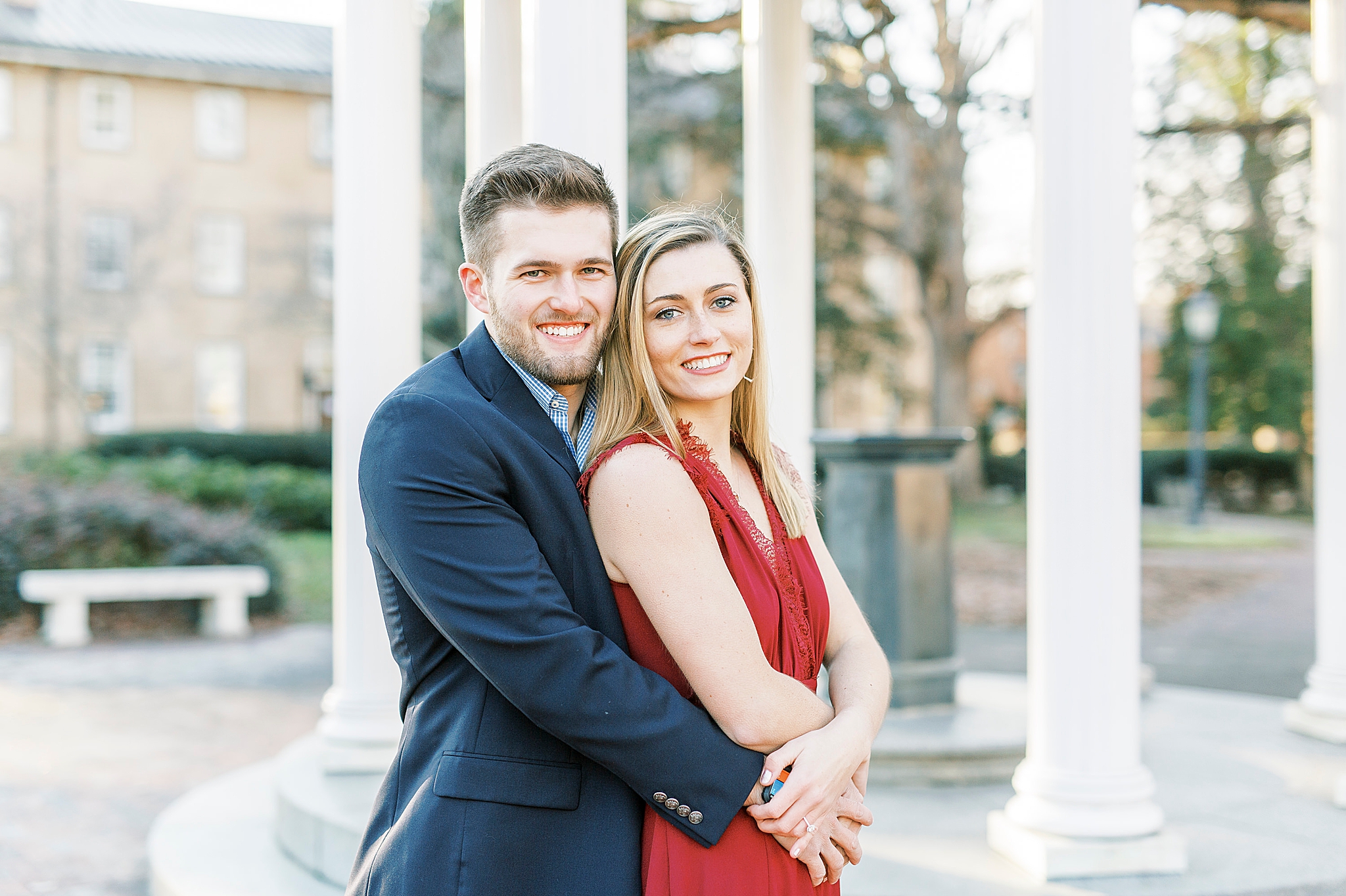 groom hugs bride from behind during winter engagement photos by gazebo