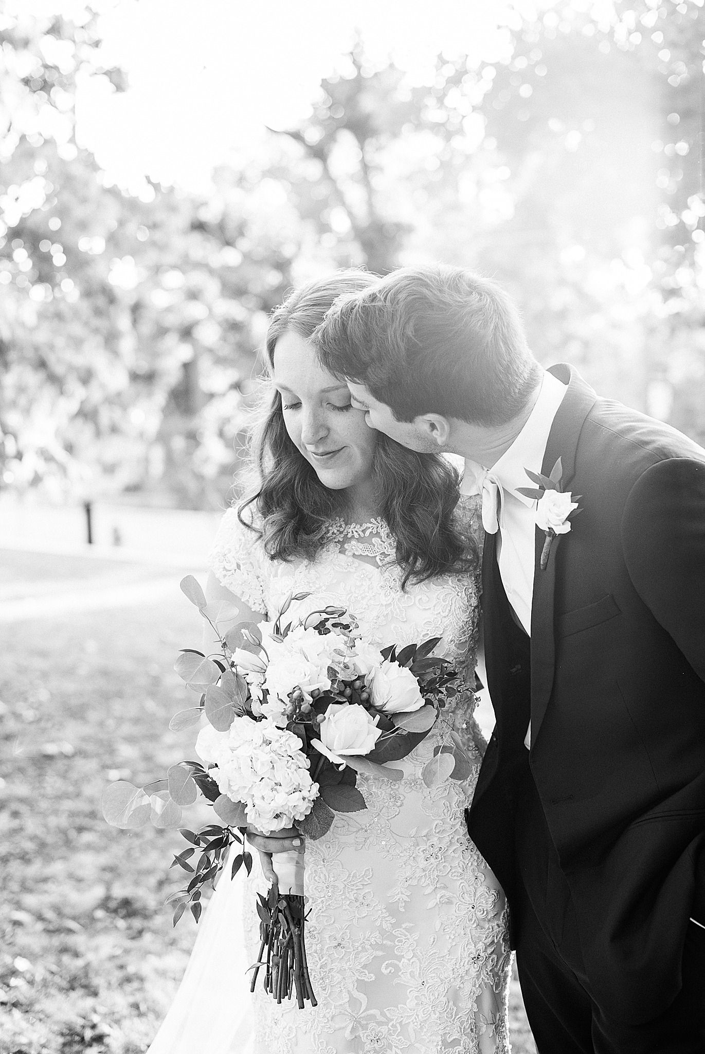 groom leans and kisses bride's cheek during classic Southern wedding portraits