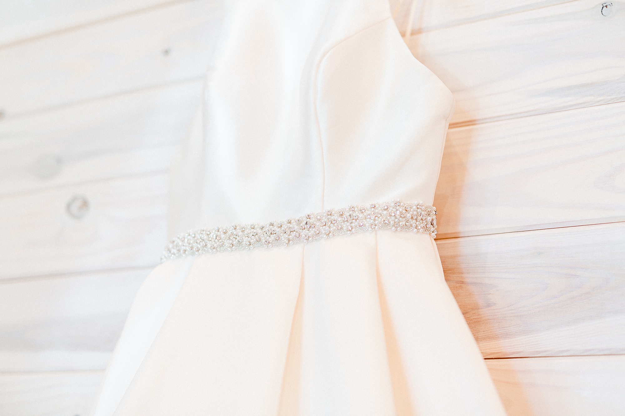 bride's modern dress hangs against wooden wall