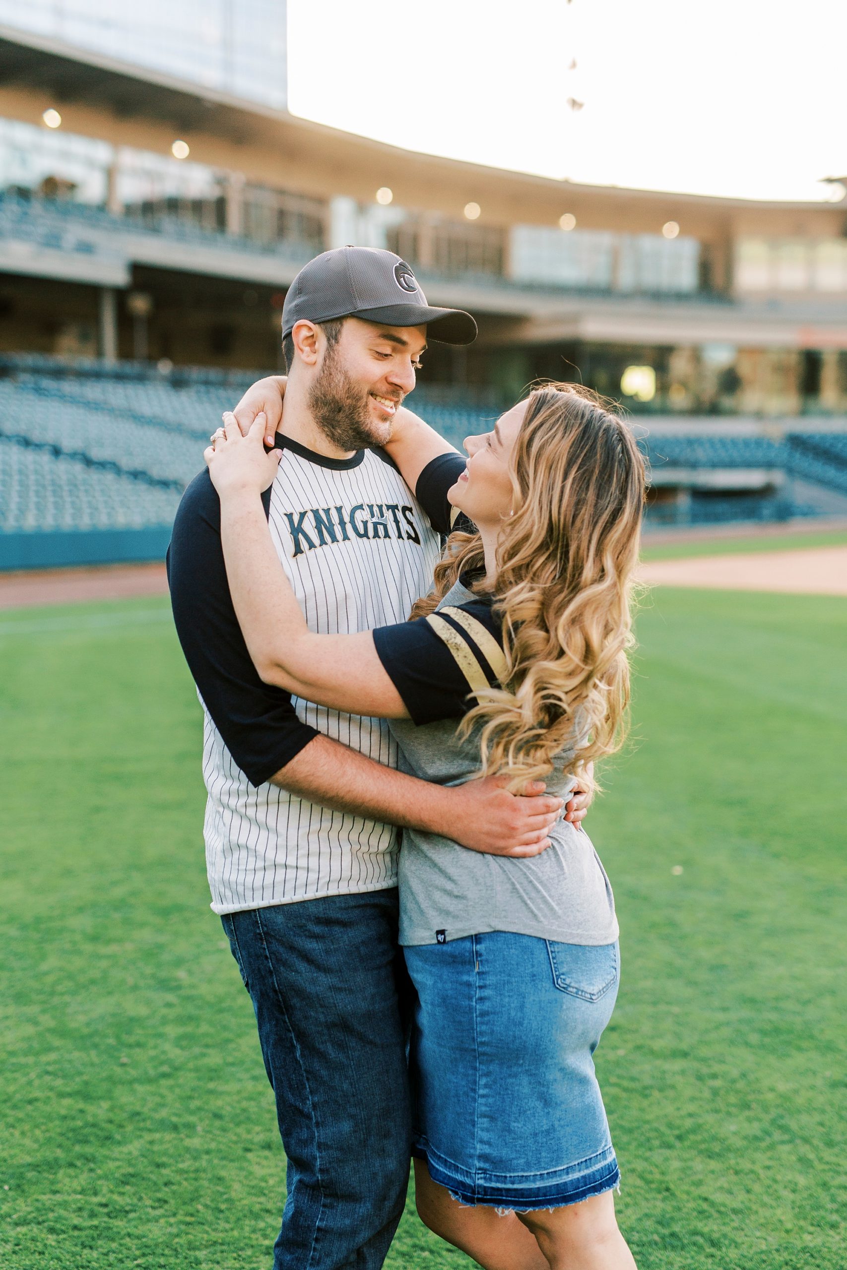 engaged couple hugs on the baseball field at Truist Field