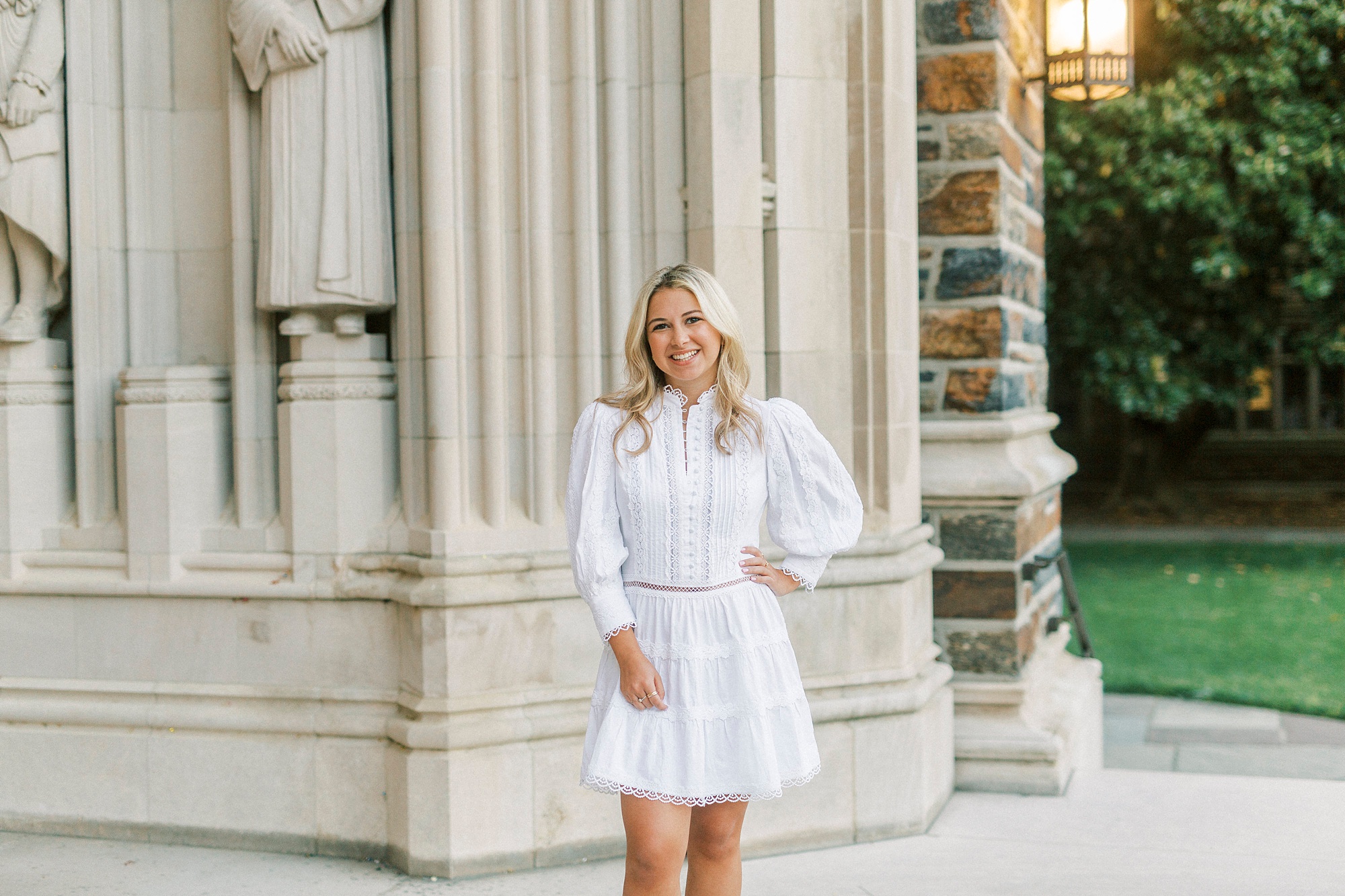 senior in white dress poses by Duke Chapel